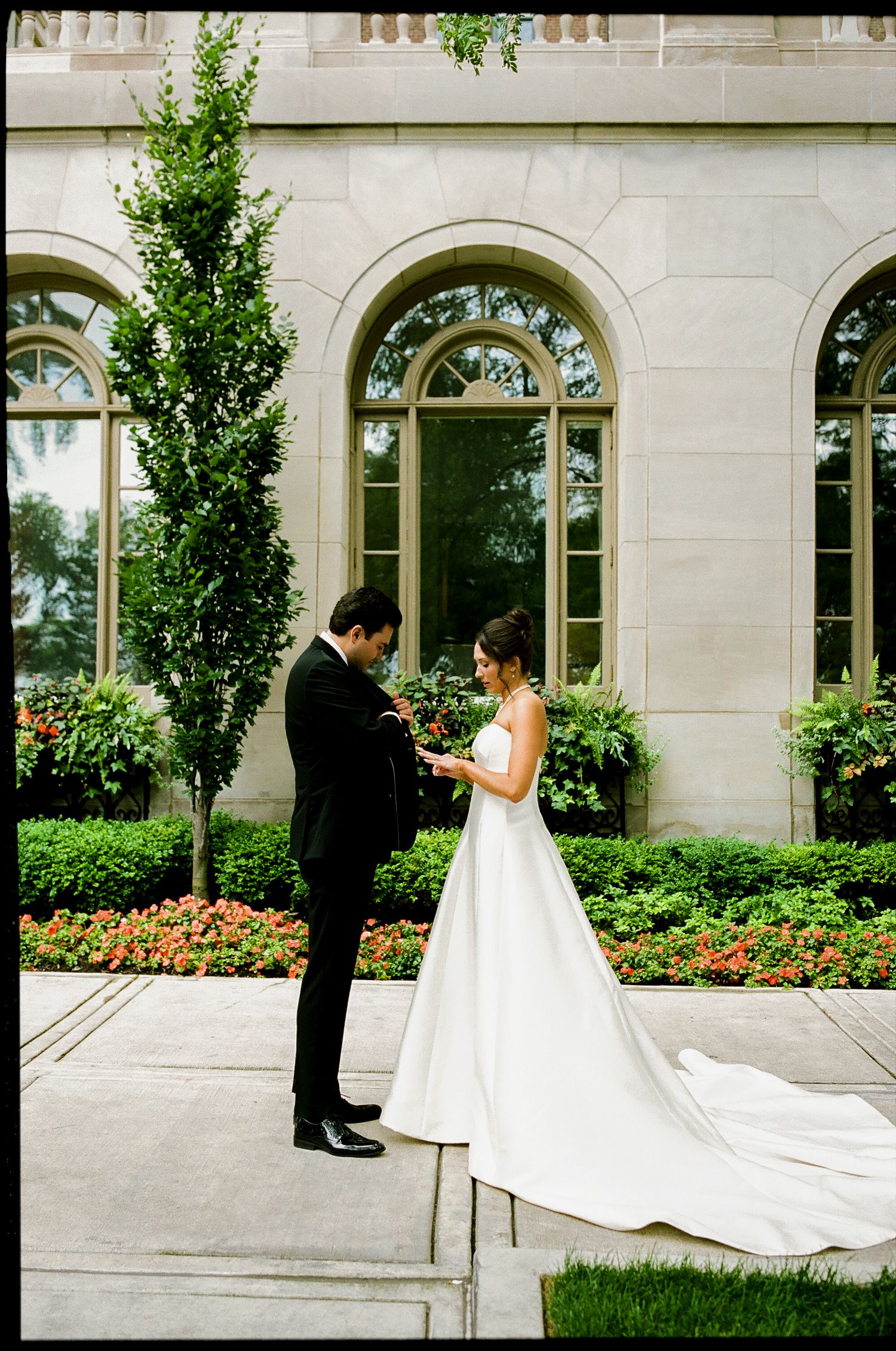 Bride and groom sharing an intimate first look moment outside a grand stone building surrounded by lush greenery.
