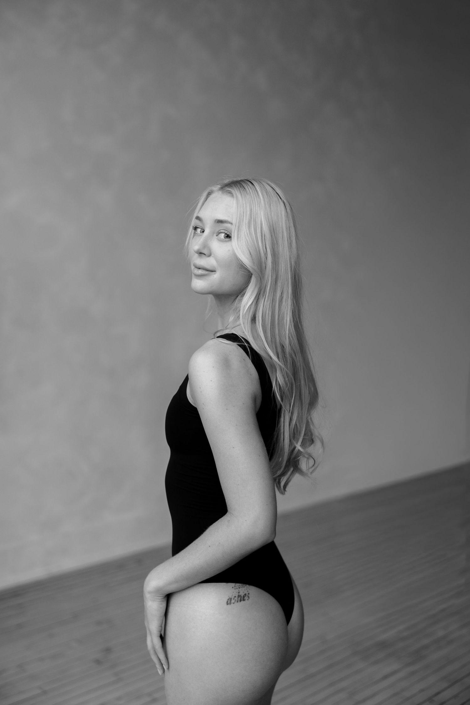A black and white portrait of a person in a black leotard posing against a studio backdrop.