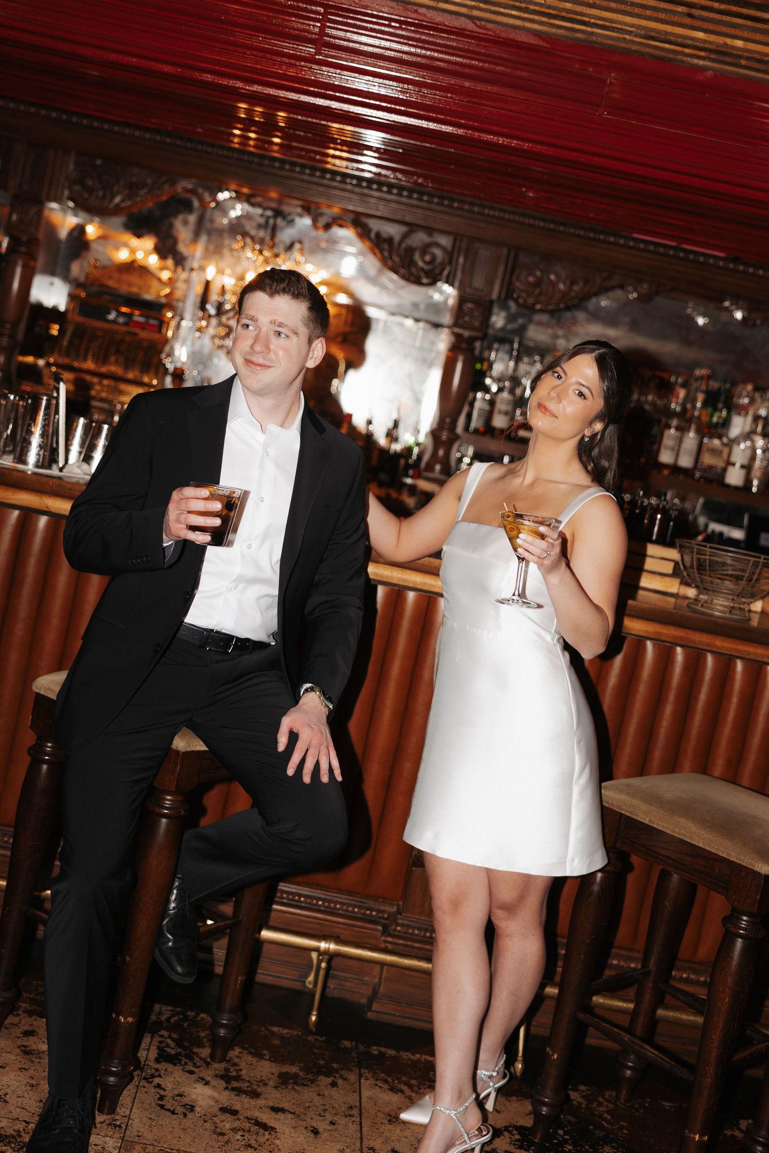 A stylish couple sharing drinks and laughing together at an upscale bar with vintage decor.