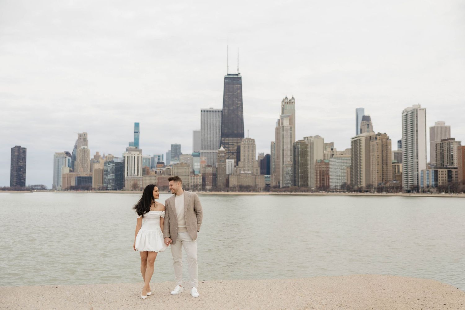 Couple poses romantically on Chicago lakefront with iconic city skyline and John Hancock Tower in background.