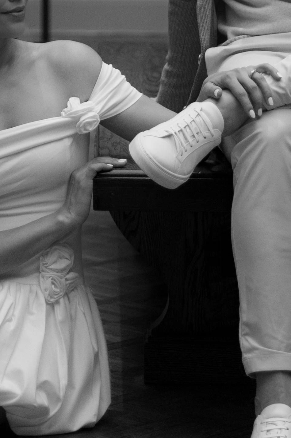 Black and white photo of a bride in white dress holding a baby wearing tiny white sneakers at a wedding celebration.