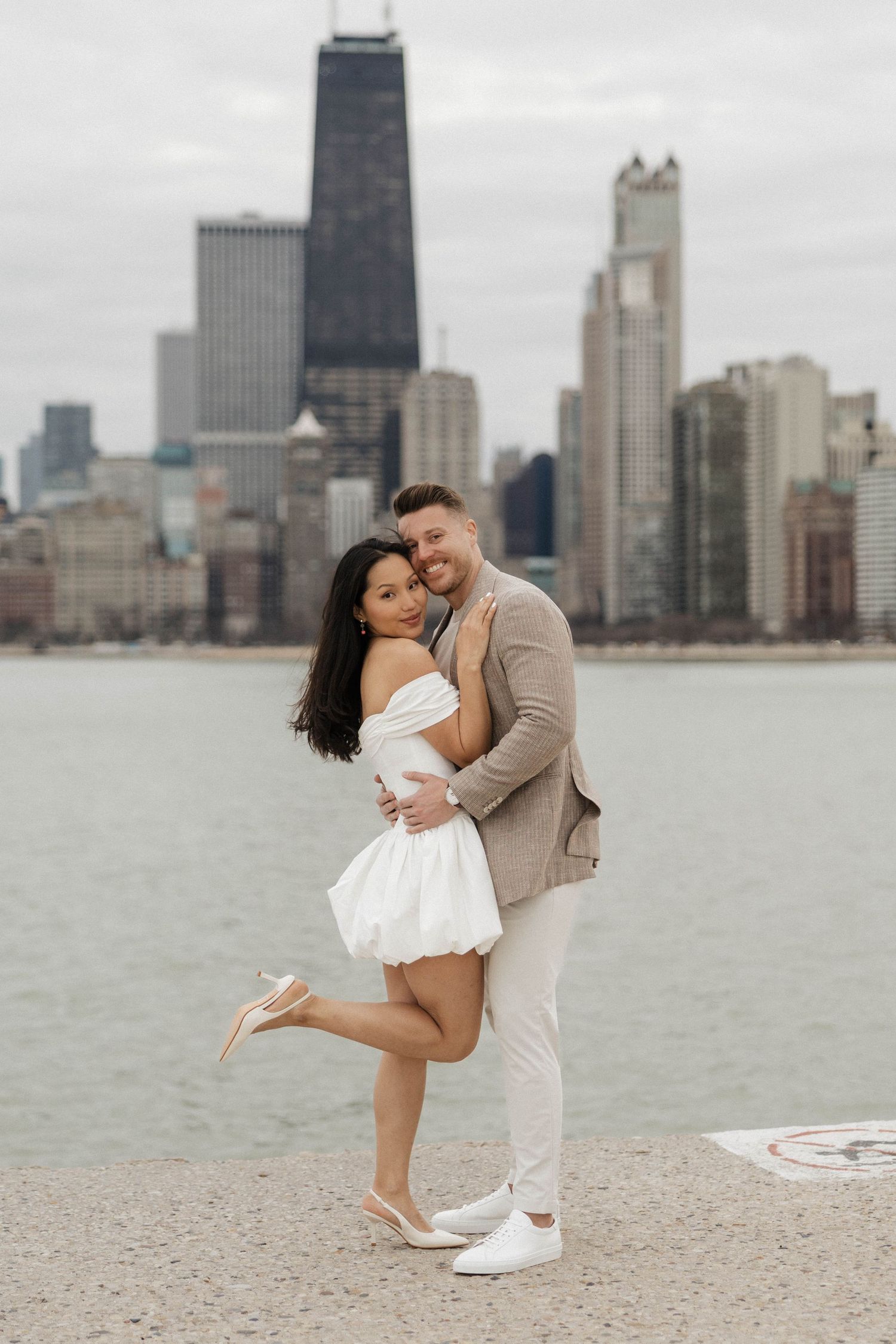 Couple embracing and smiling by Chicago lakefront with city skyline backdrop.