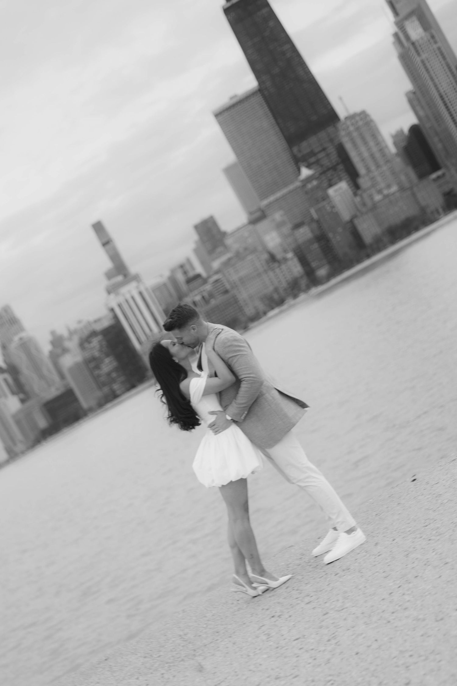 Black and white photo of a couple kissing on a beach with the Chicago skyline in the background.
