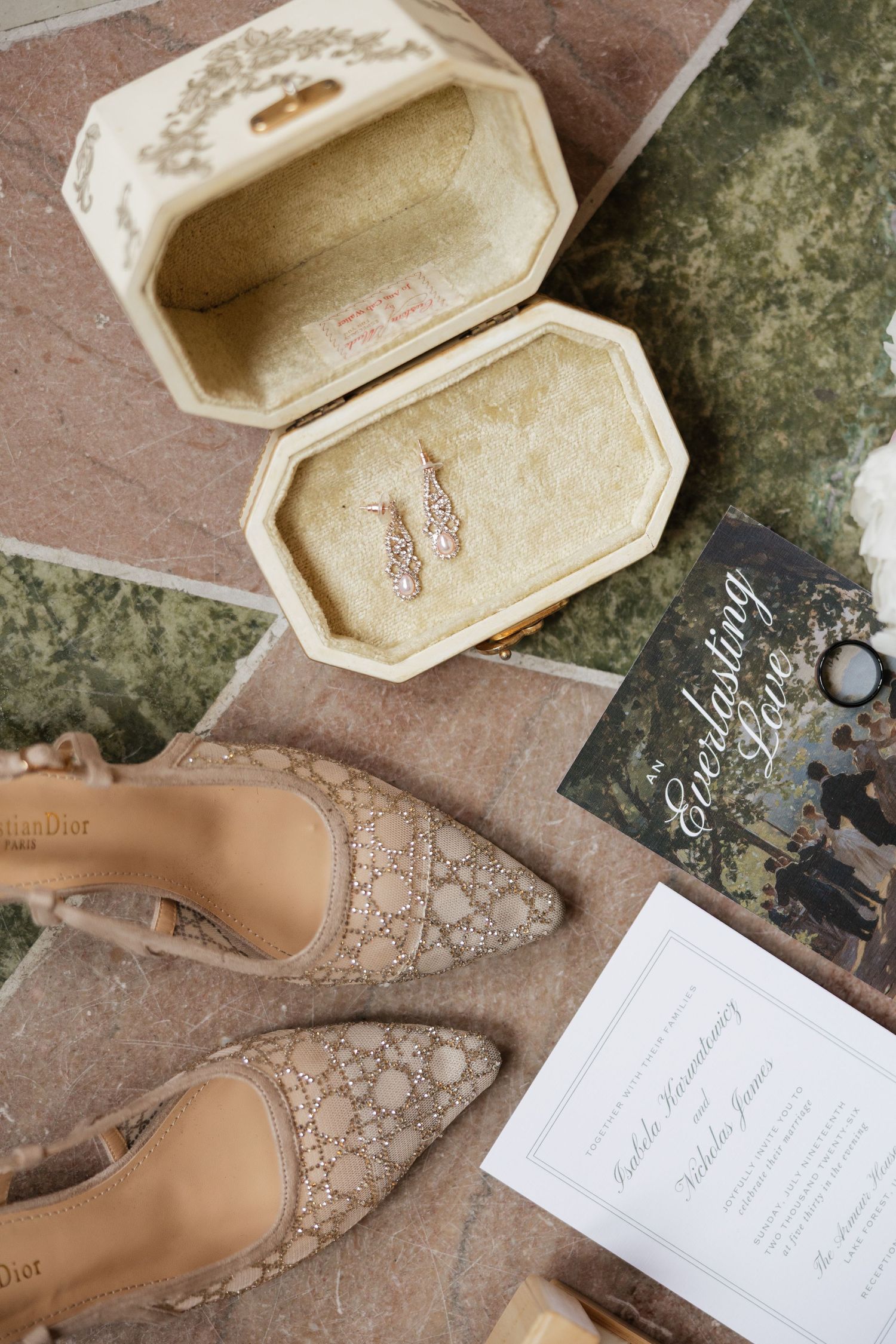 Christian Dior lace heels beside an ivory ring box with earrings and elegant wedding stationery on a tiled surface.