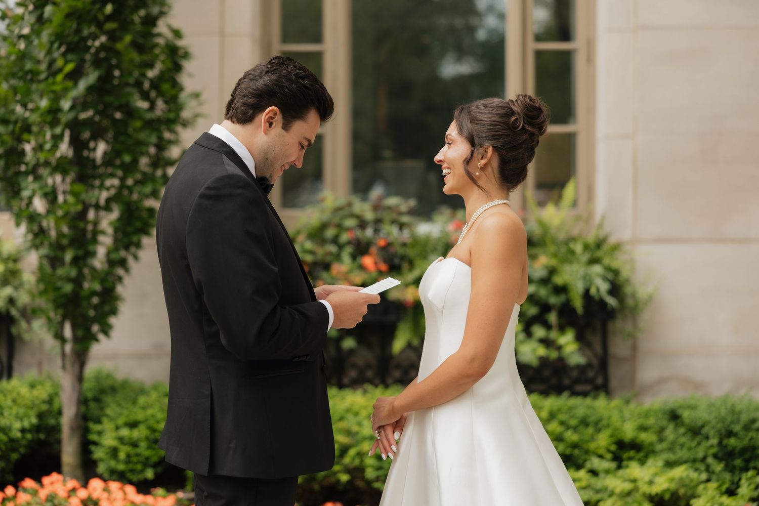 Bride and groom exchange personal vows outdoors, surrounded by lush greenery and flowers during intimate wedding ceremony.