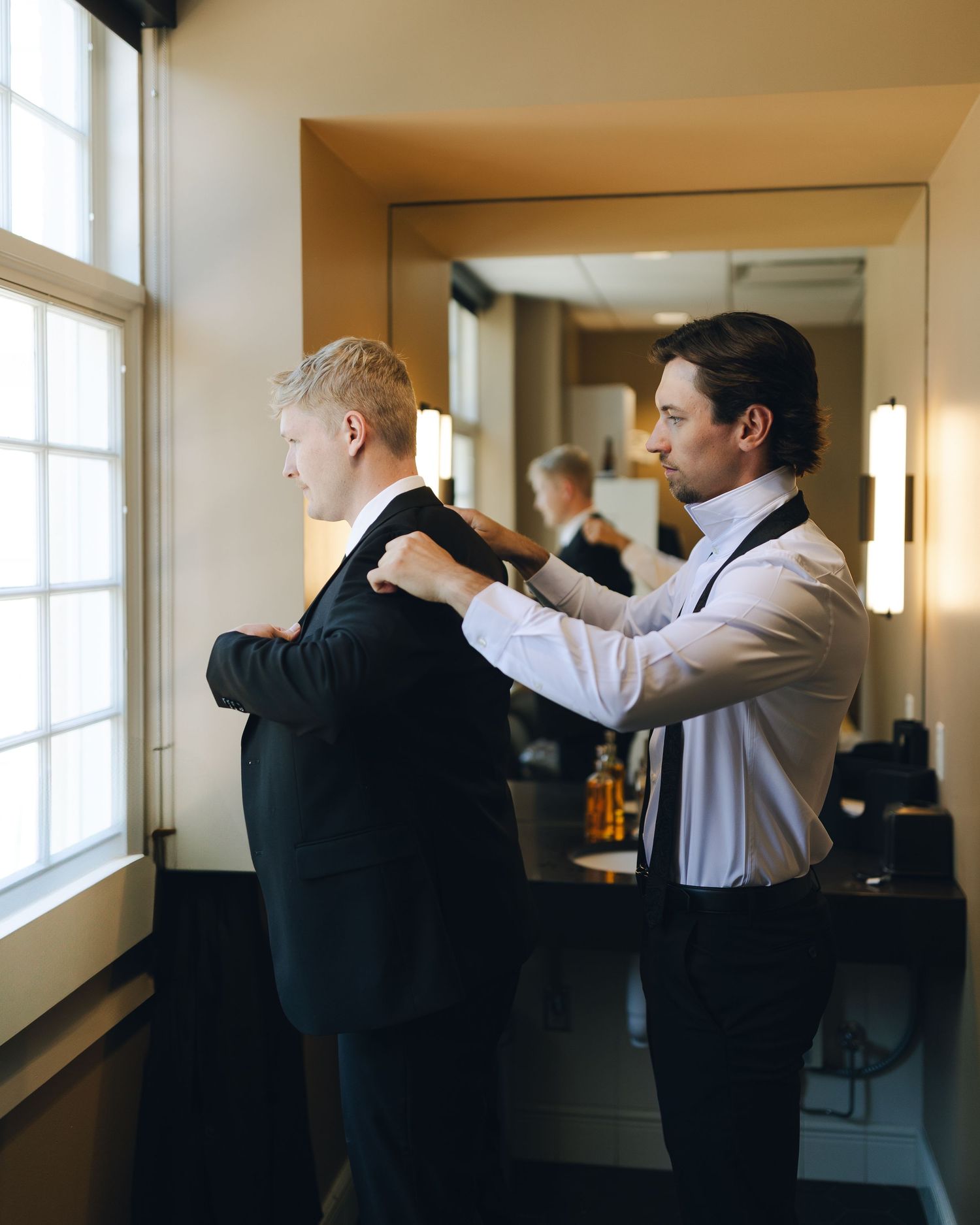 Groomsmen helping each other prepare and adjust formal attire before ceremony.