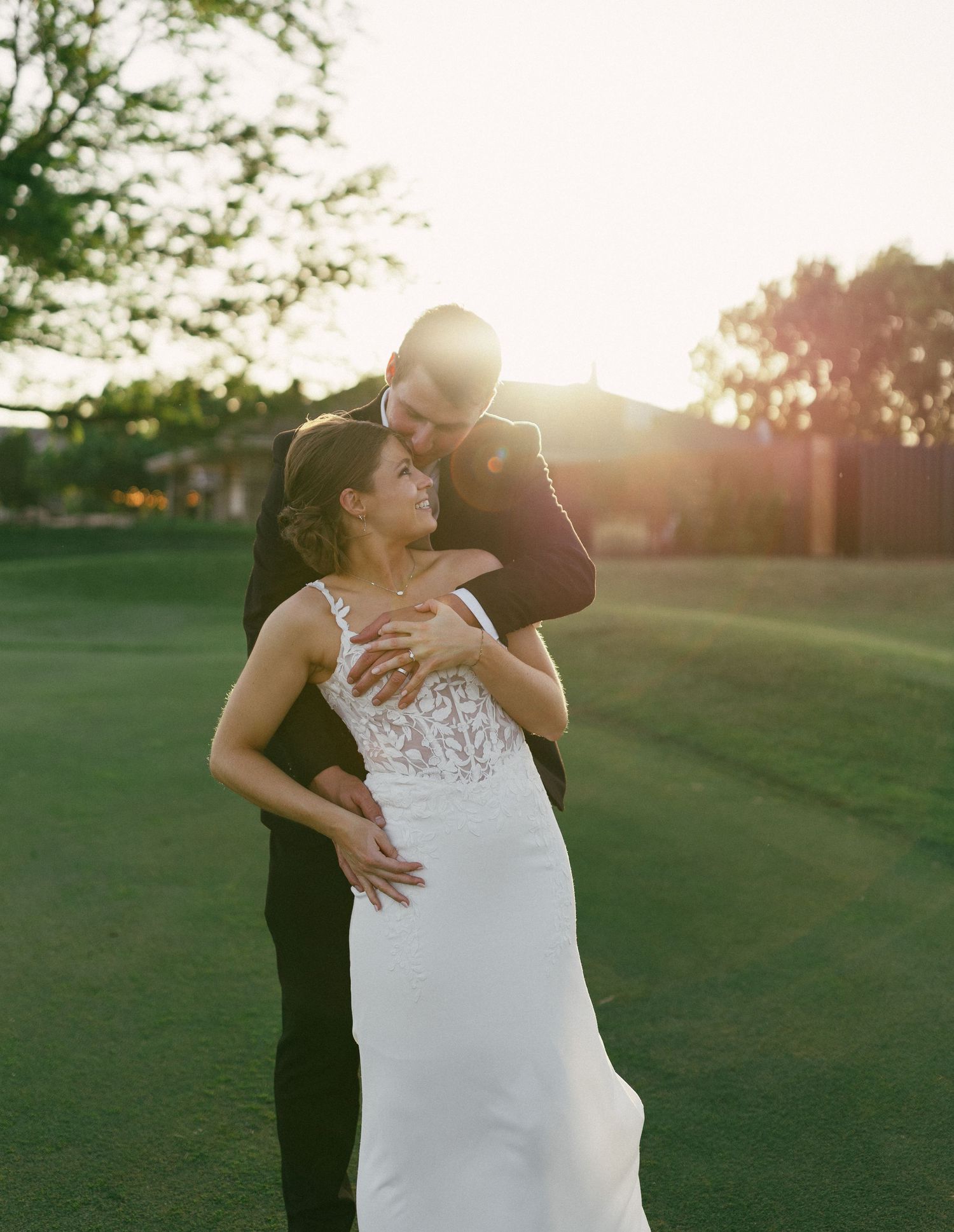 Couple embracing on a green lawn during golden hour sunset.