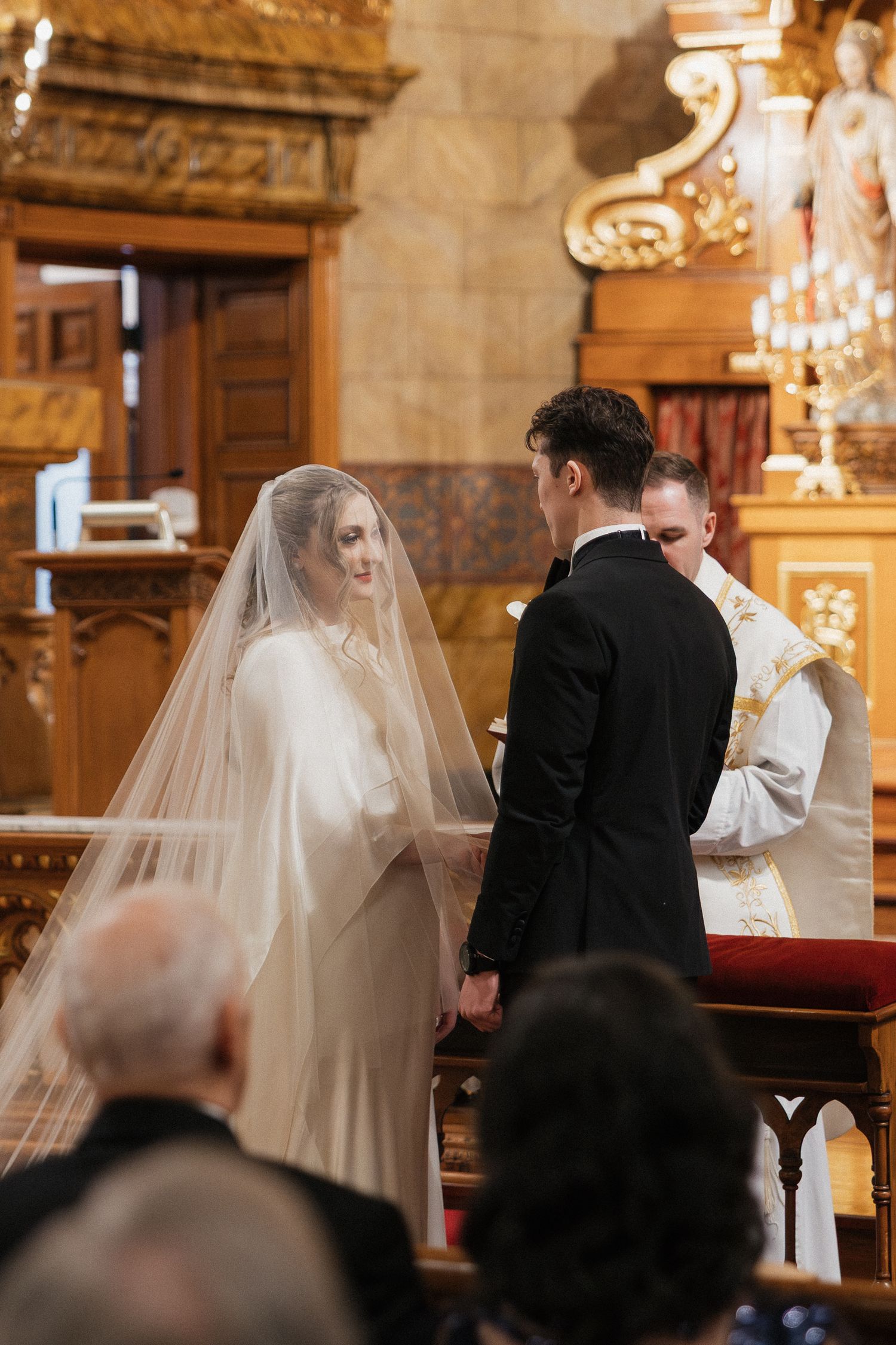 Traditional church wedding ceremony with couple at altar under chandeliers.
