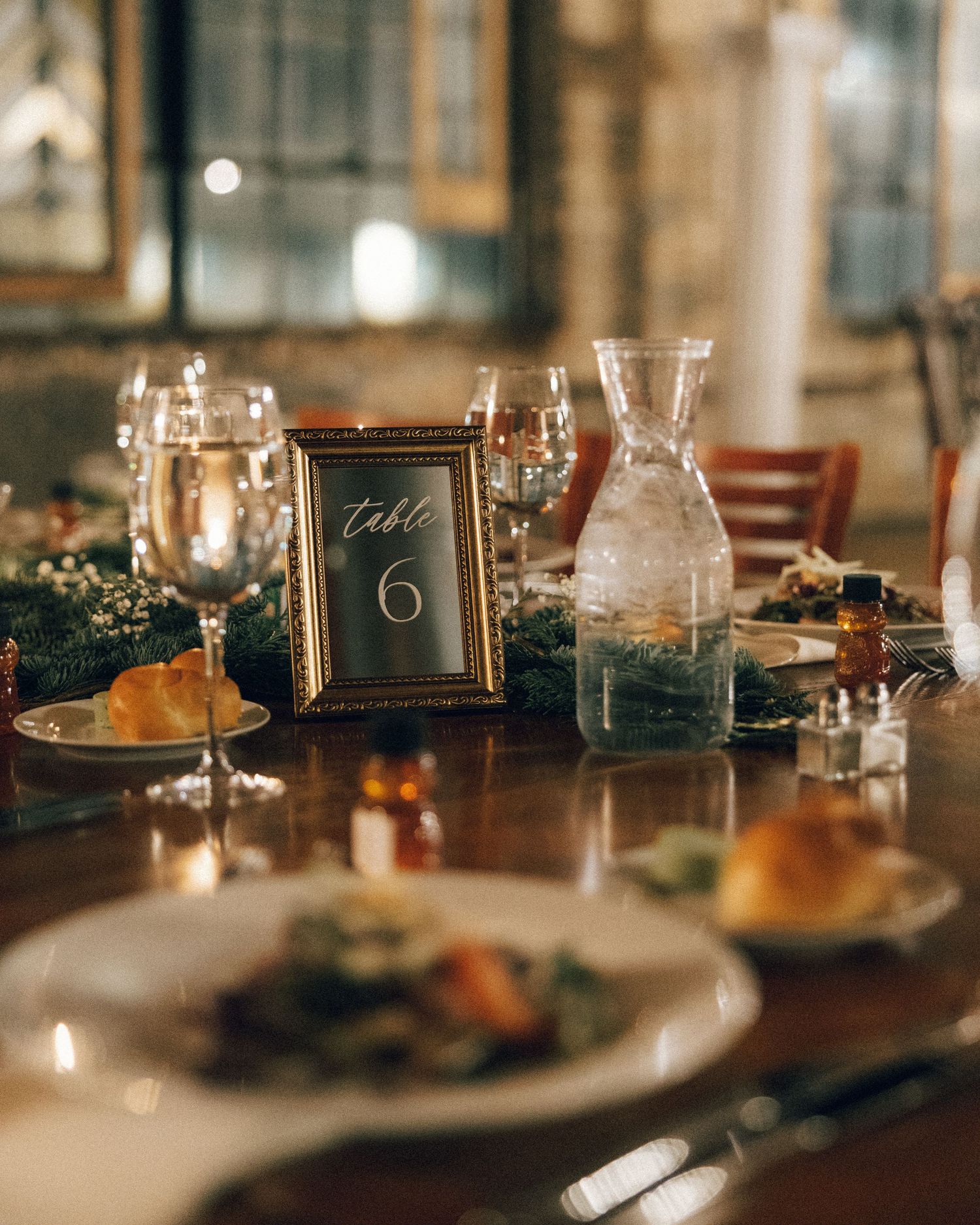 Elegant wedding table setting with candlelight, vintage frames, and rustic greenery decorations in warm ambient lighting.