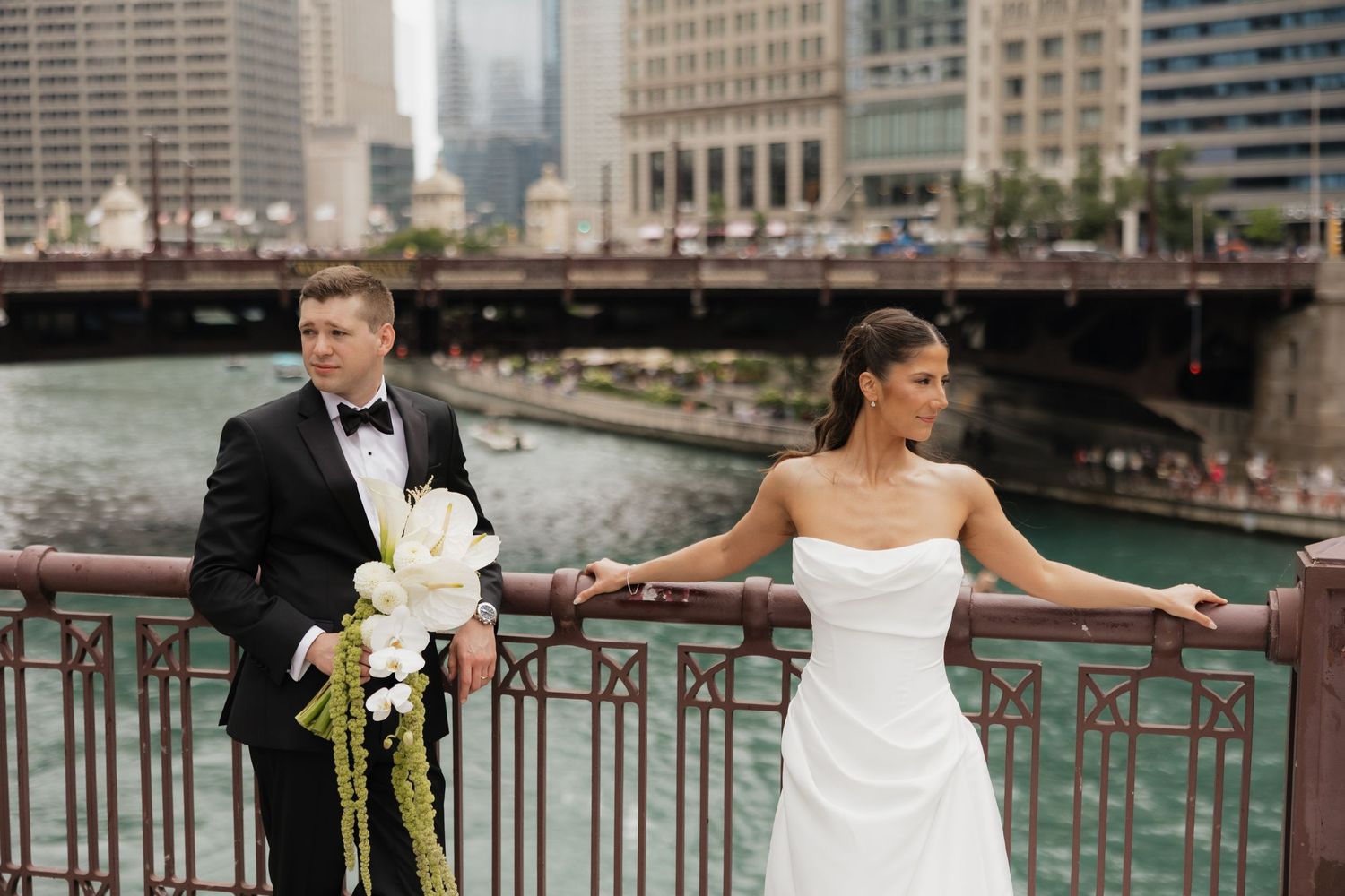 Bride and groom posing on a bridge over the Chicago River with city skyline in the background on their wedding day.
