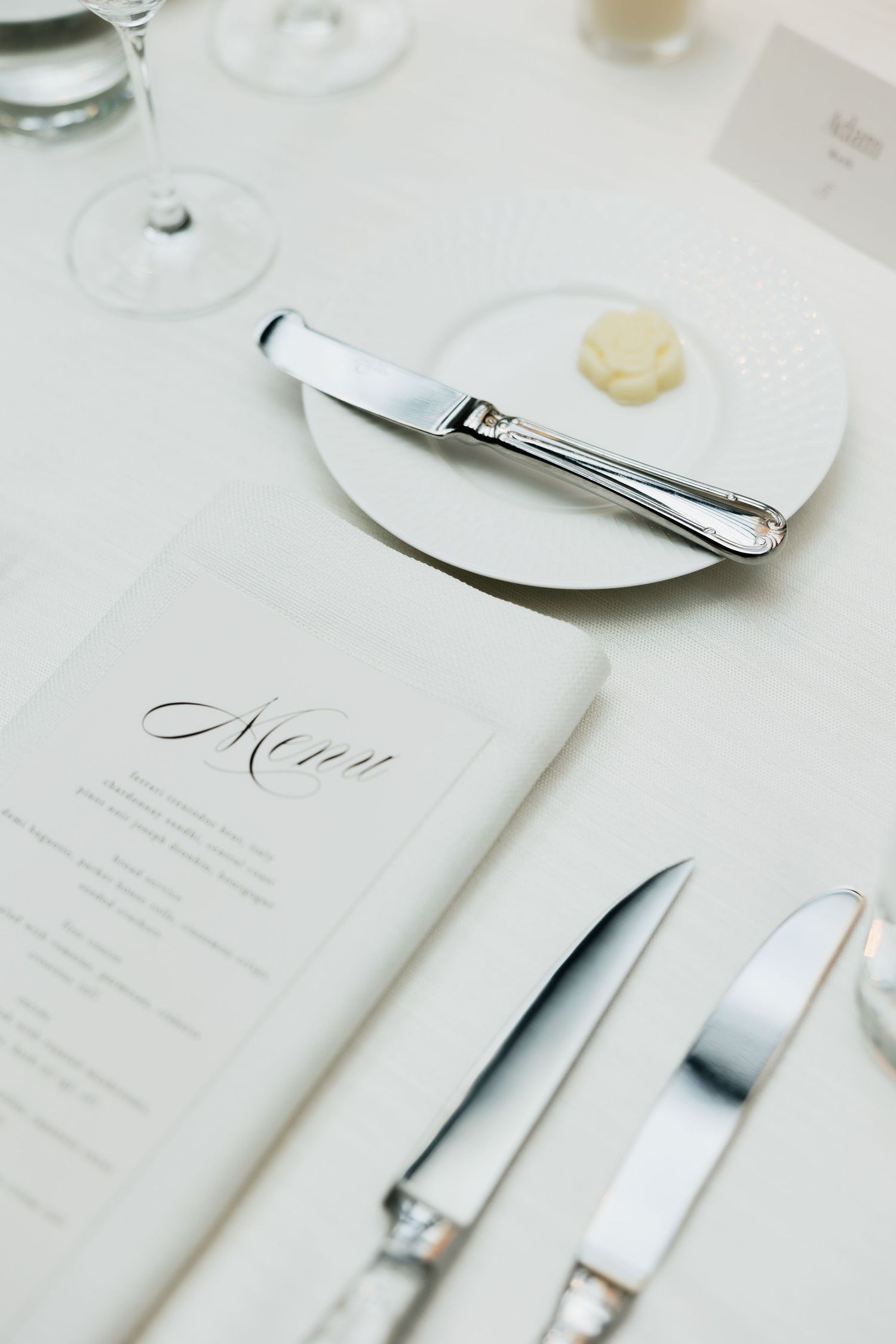 Elegant wedding table setting with a calligraphy menu card, silver cutlery, bread plate with butter, and crystal glassware.
