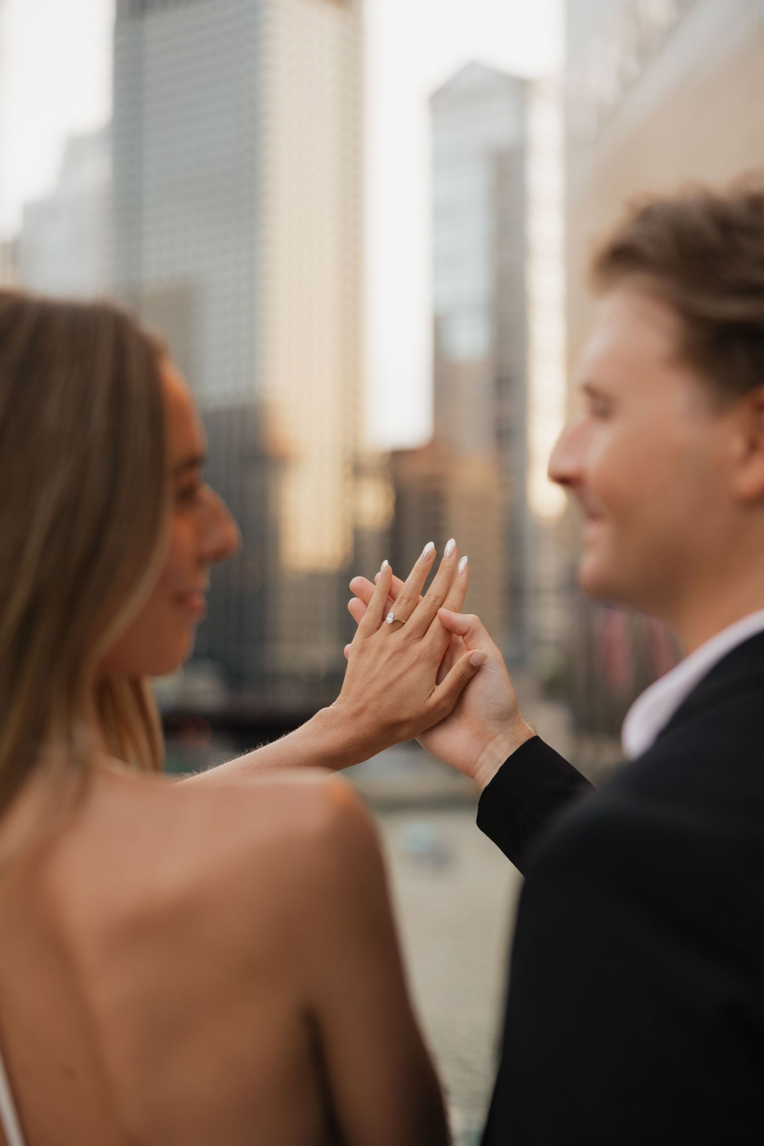 Couple admiring engagement ring with city skyline backdrop, celebrating their engagement in urban setting.