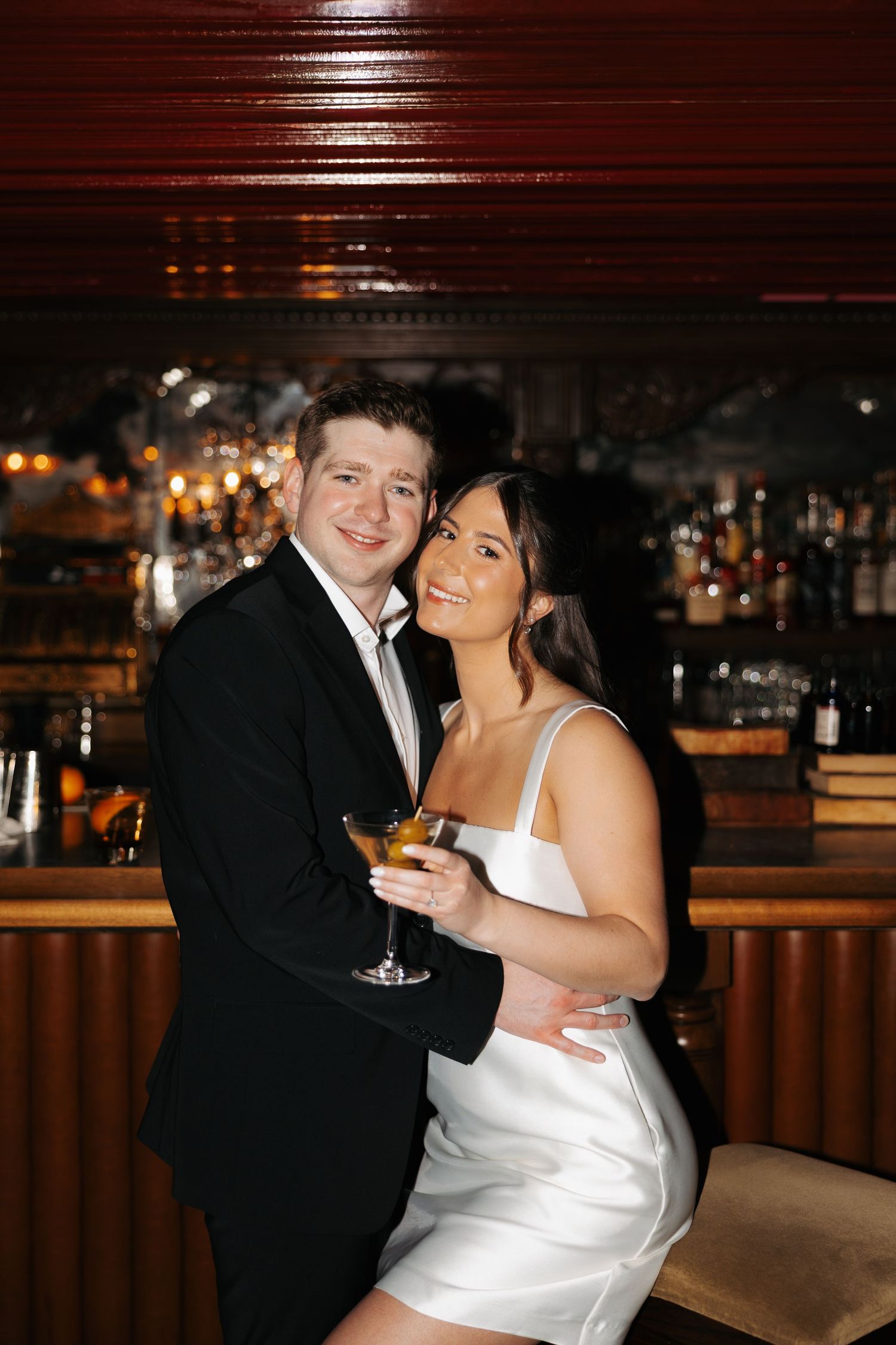 Newlywed couple shares an intimate moment at a dimly lit bar with wine glasses.