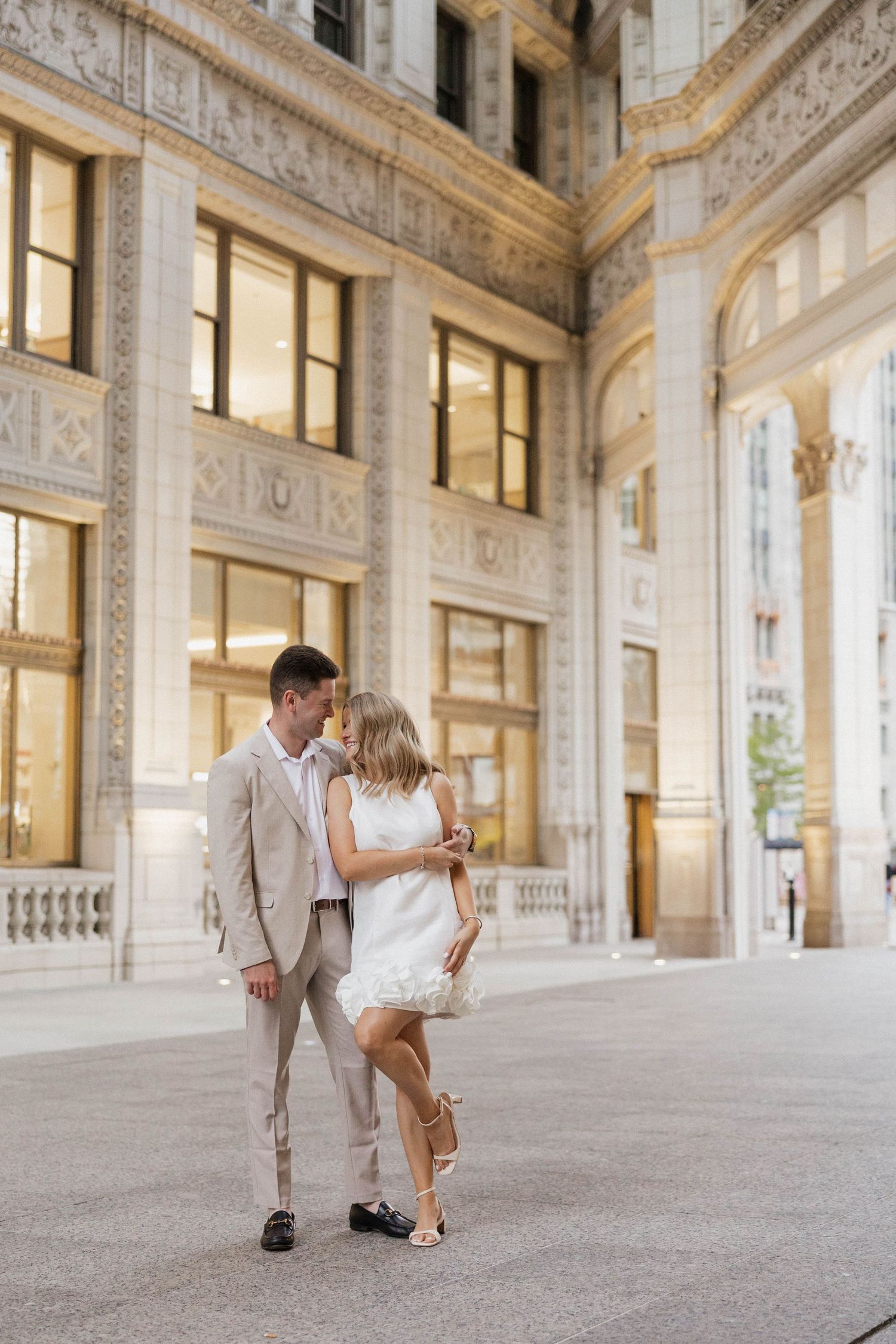 Couple shares romantic moment outside ornate Chicago building in coordinating beige and white outfits.