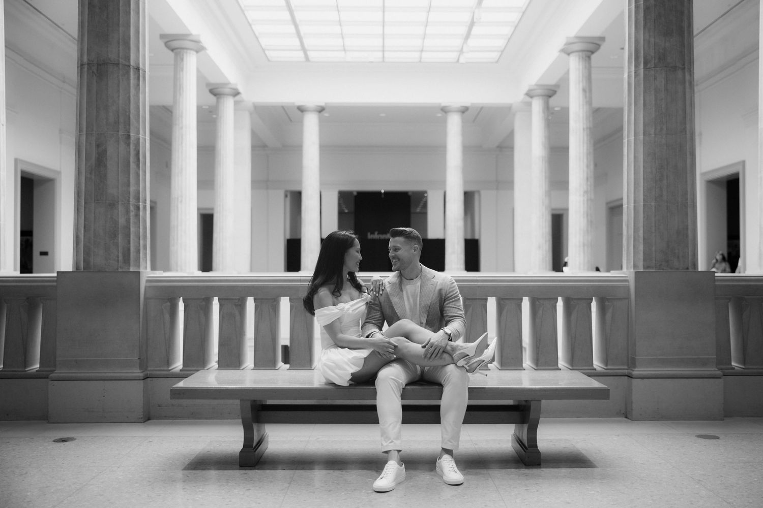 Black and white photo of a couple sitting on a bench in a grand columned interior space.
