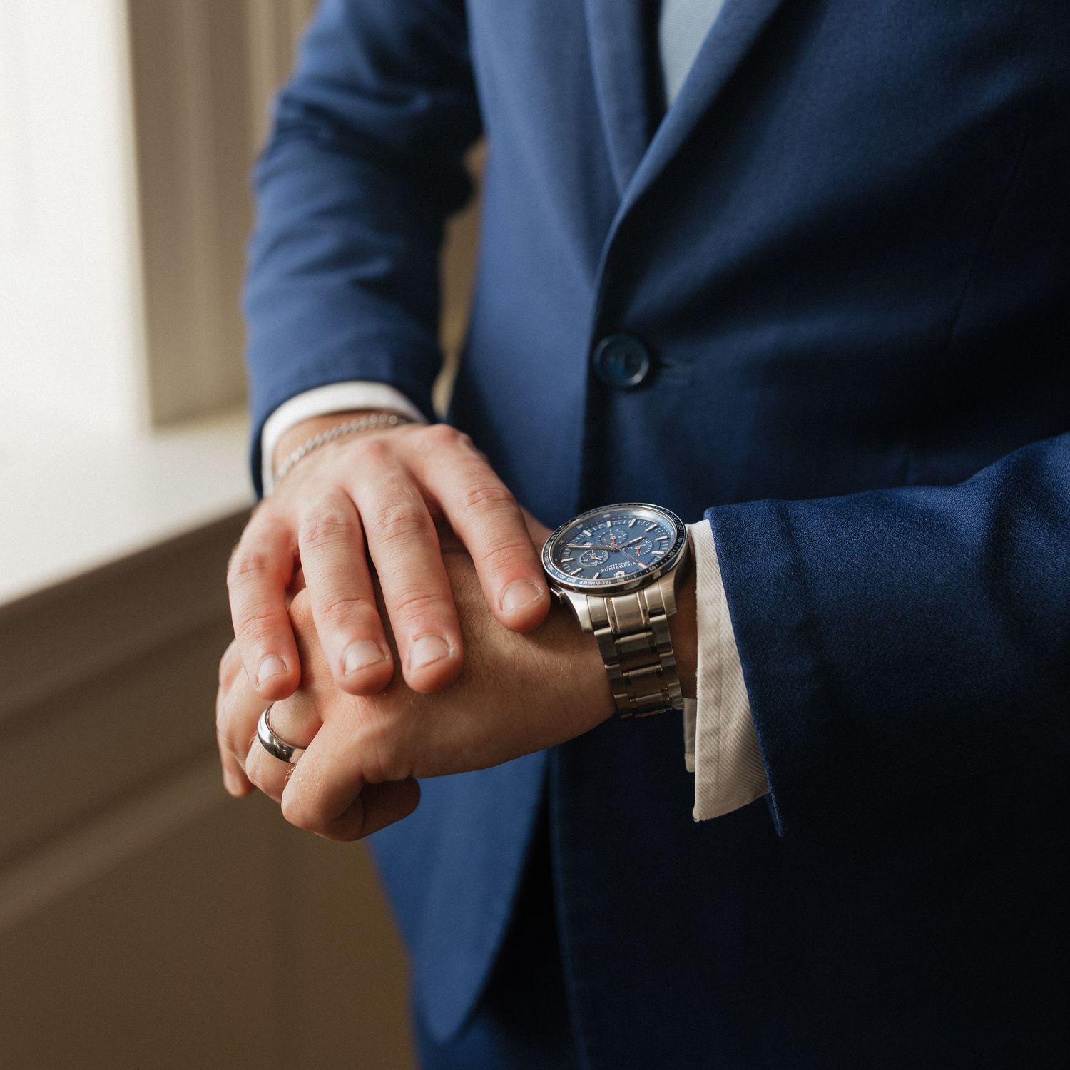 Close-up view of a person wearing a navy suit jacket checking their silver metal wristwatch.