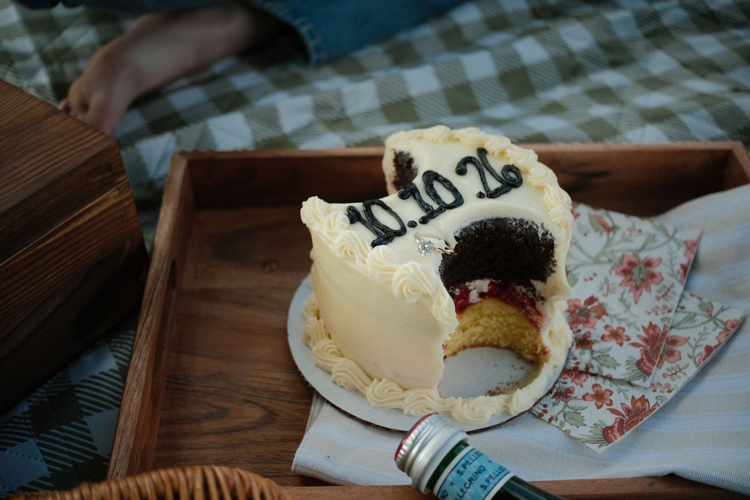 A wooden serving tray holds a partially eaten bagel with cream cheese on a floral patterned napkin.