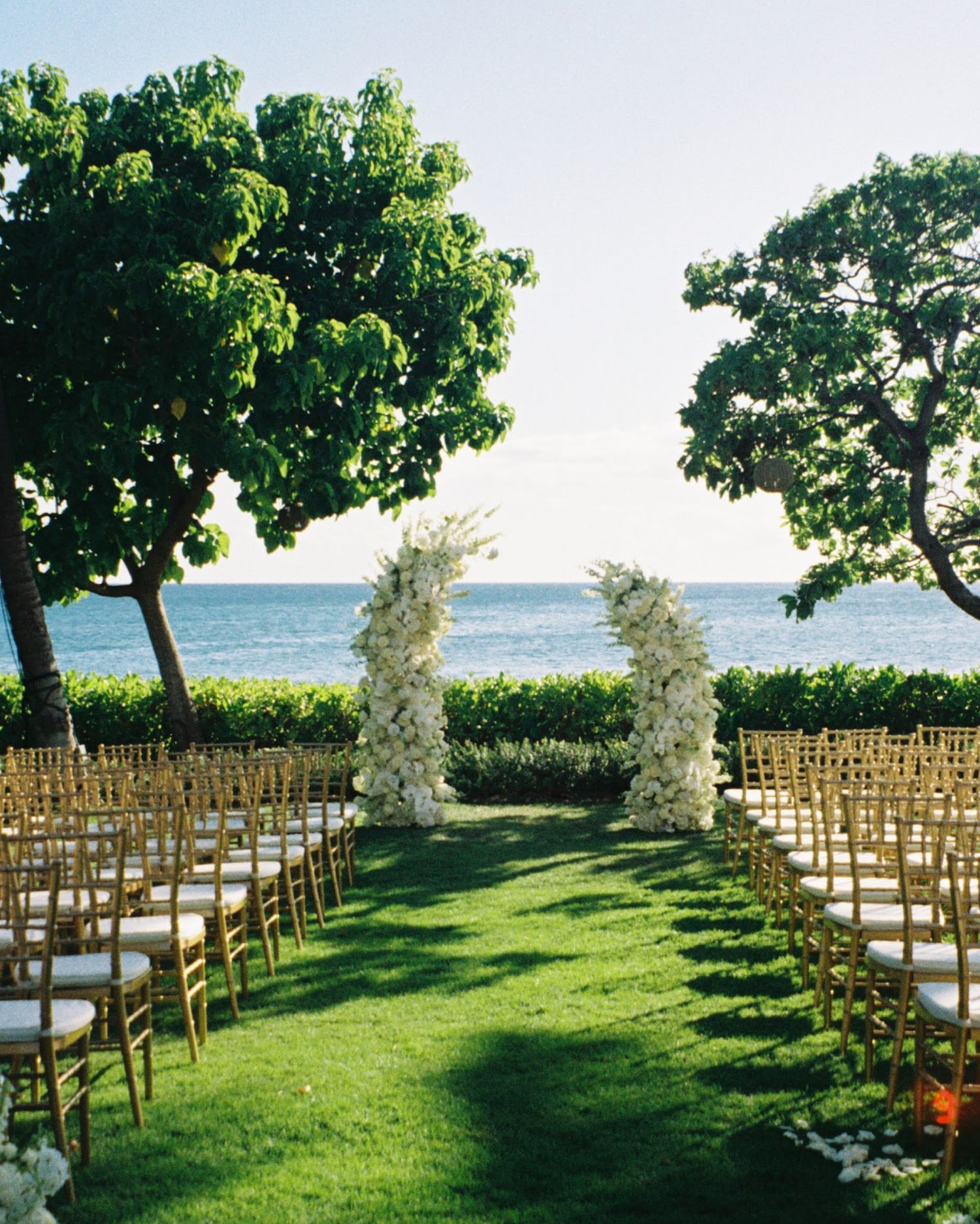Rows of wooden chairs arranged on a lush green lawn overlooking the ocean for an outdoor wedding ceremony.