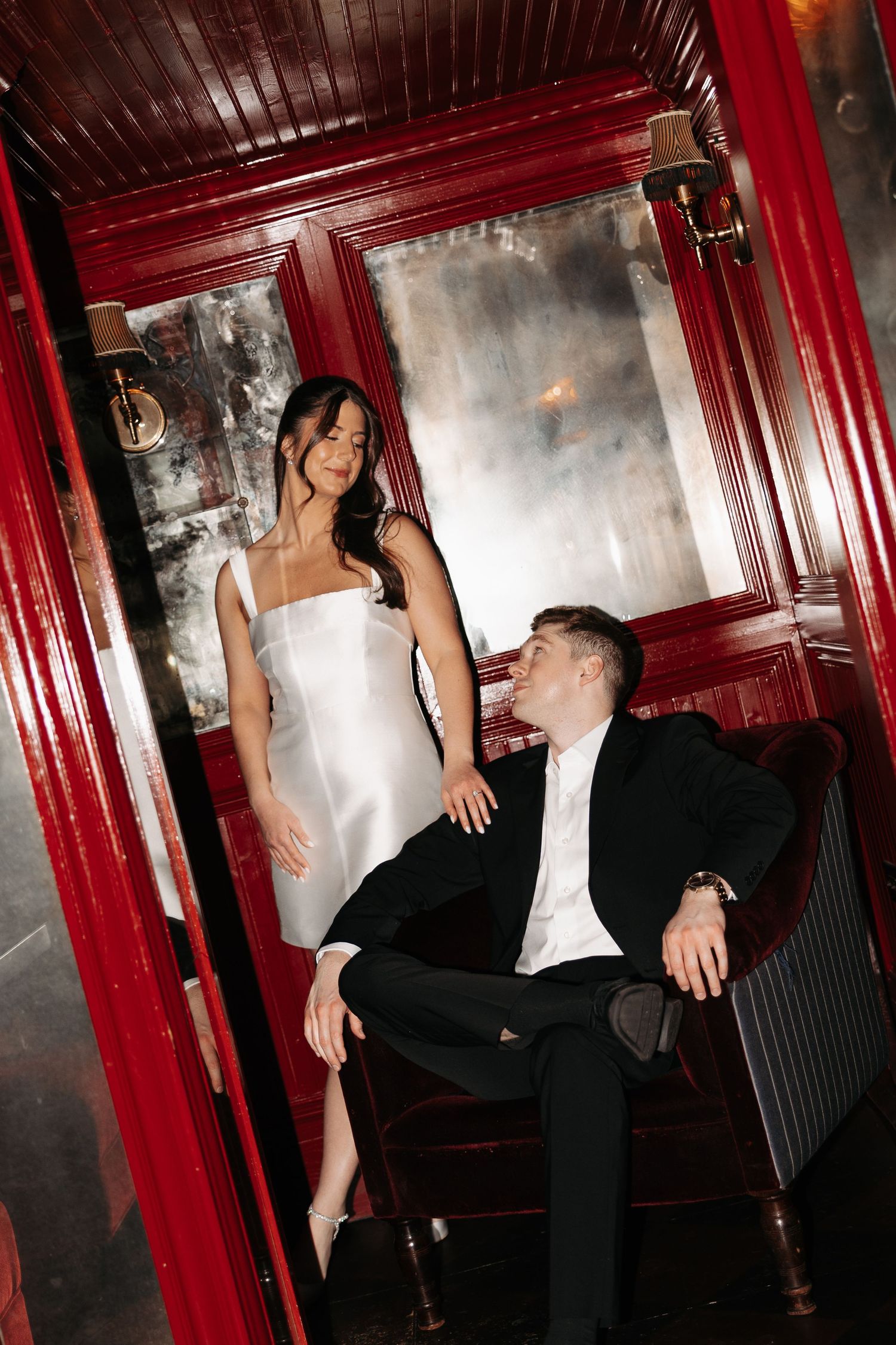People in formal attire dancing and socializing in a dimly lit venue with red walls and moody lighting.