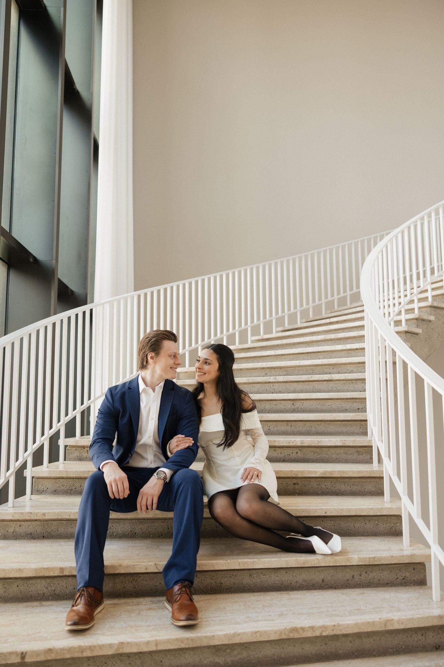 A couple sits together on modern white stairs sharing an intimate moment.