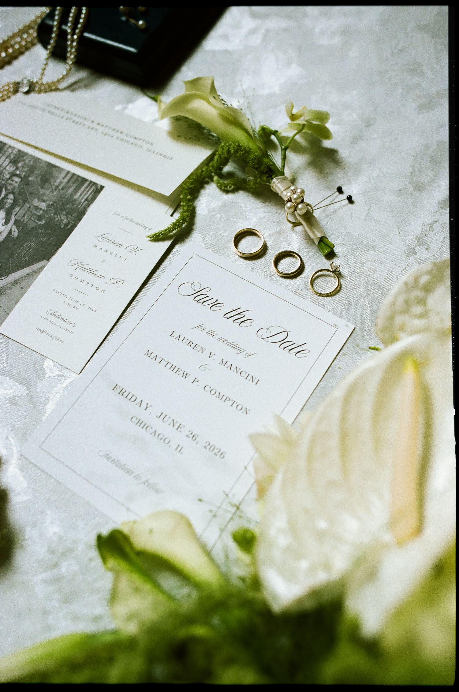 Elegant wedding save the date card with gold rings, floral boutonniere, and stationery suite on marble surface.