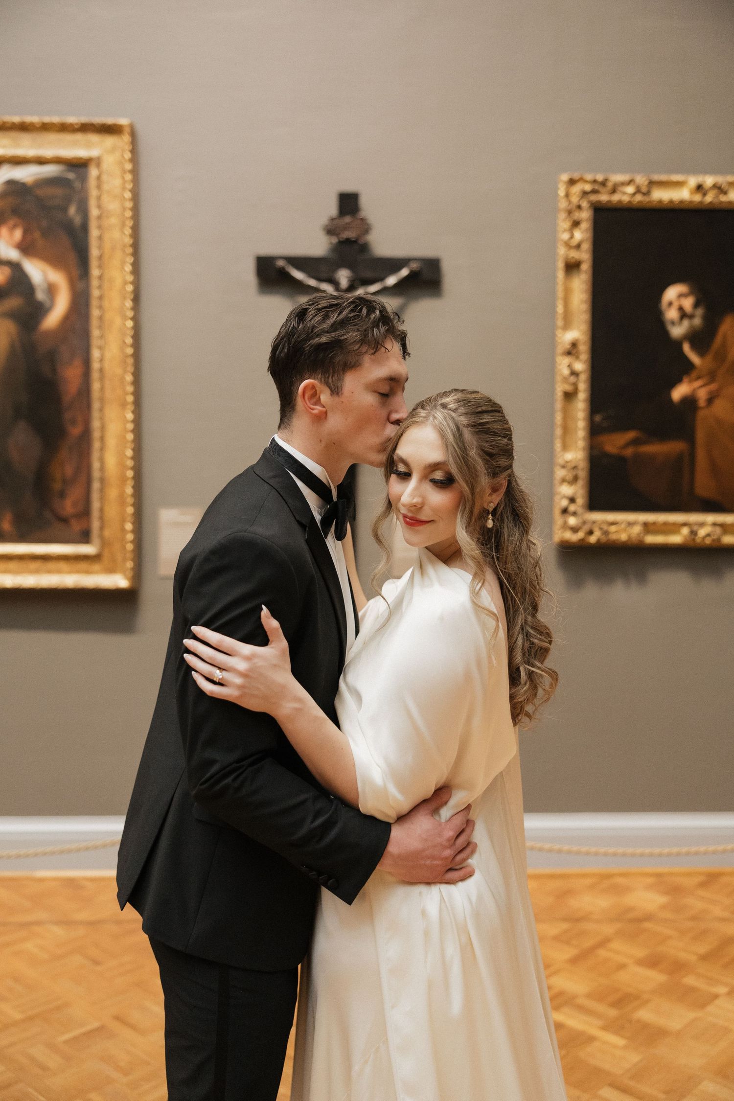 A couple shares intimate moments in an art gallery with gold-framed paintings.