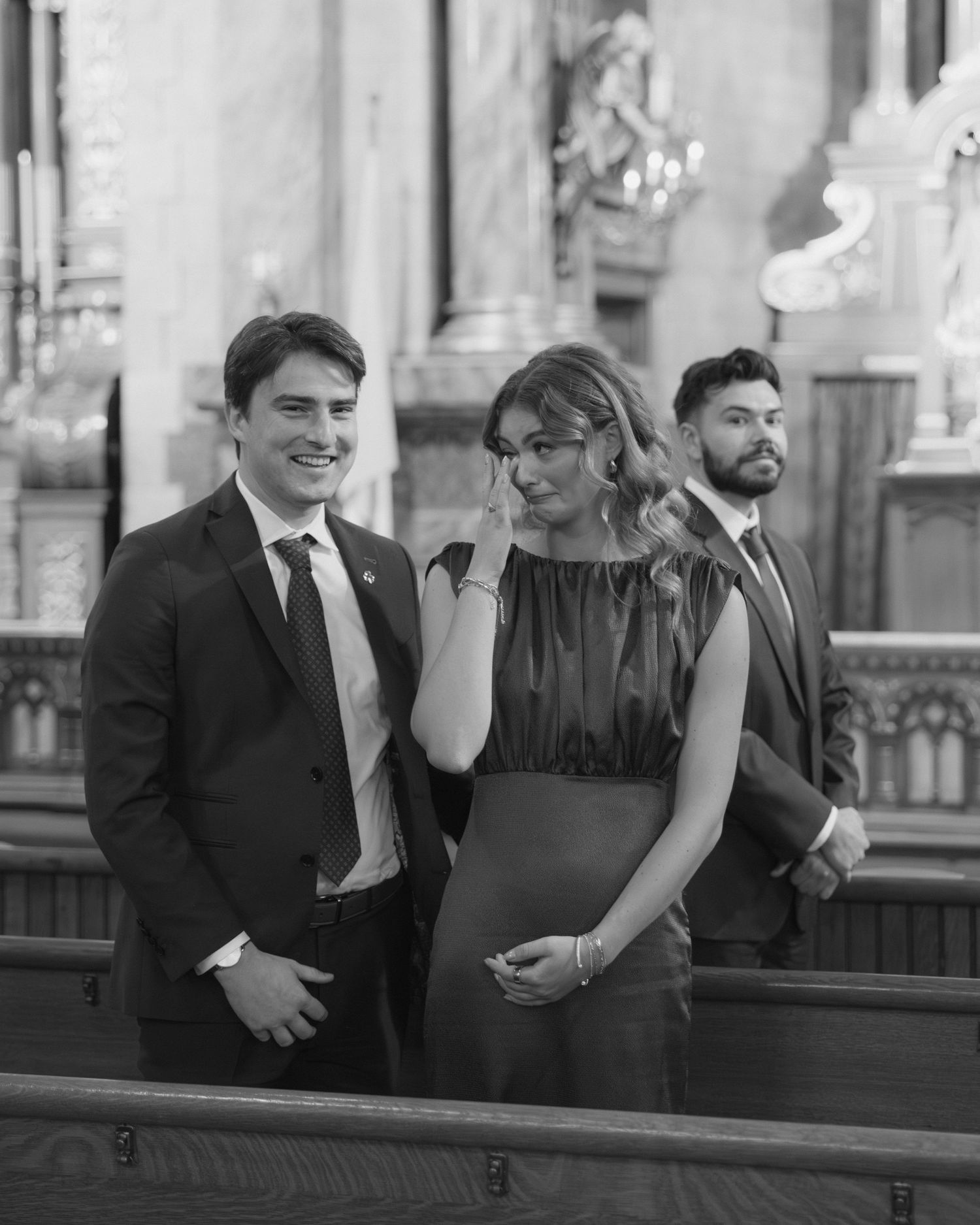A group in formal attire stands together in black and white photography at an elegant venue.