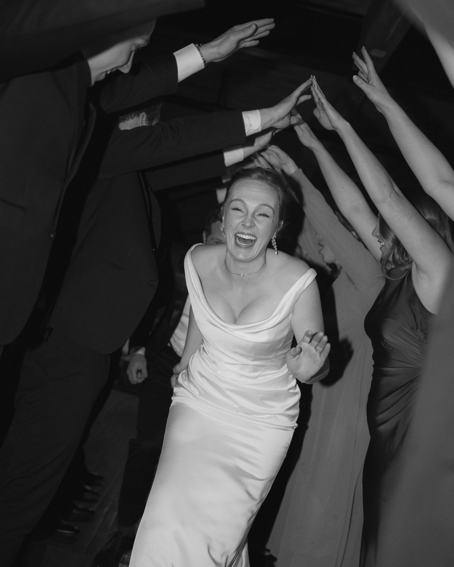 A joyful woman in a white dress dances with raised arms while others' hands are visible in the background.