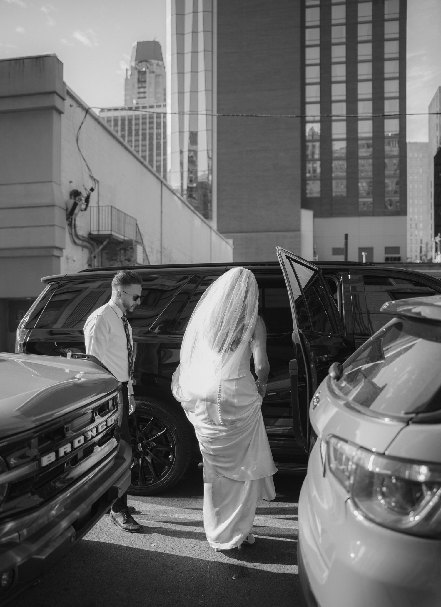 A sequence of black and white photos showing a person in protective gear inspecting and cleaning a parked vehicle.
