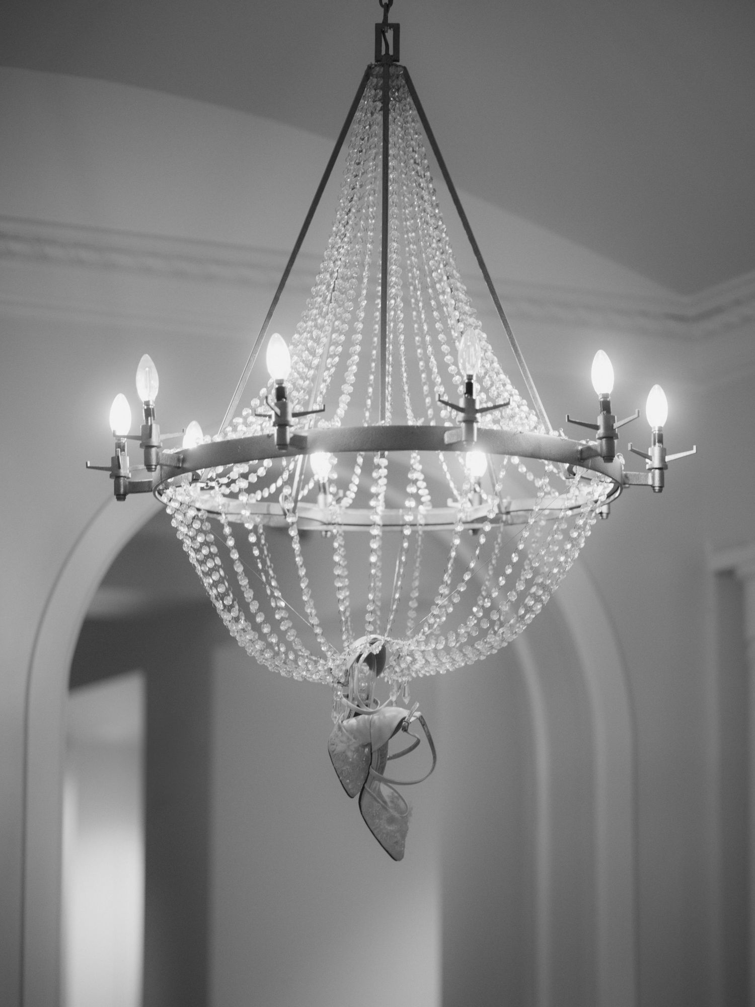Elegant crystal chandelier photographed in black and white showing dramatic shadows and light patterns on ceiling.
