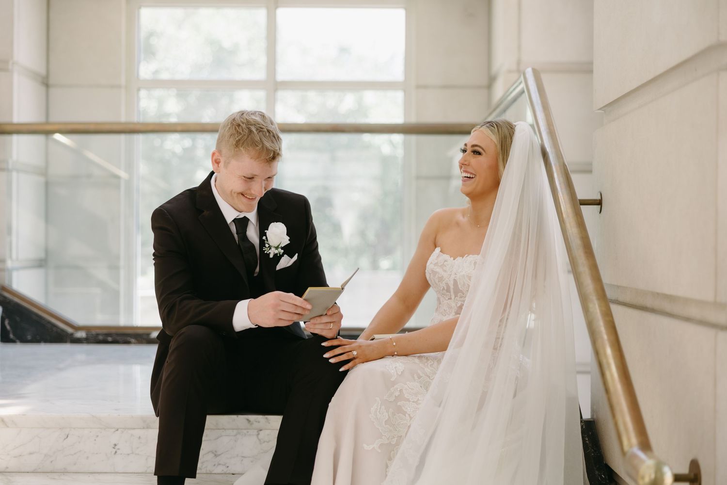 A bride and groom share an intimate first look moment in a bright sunlit room with white walls.