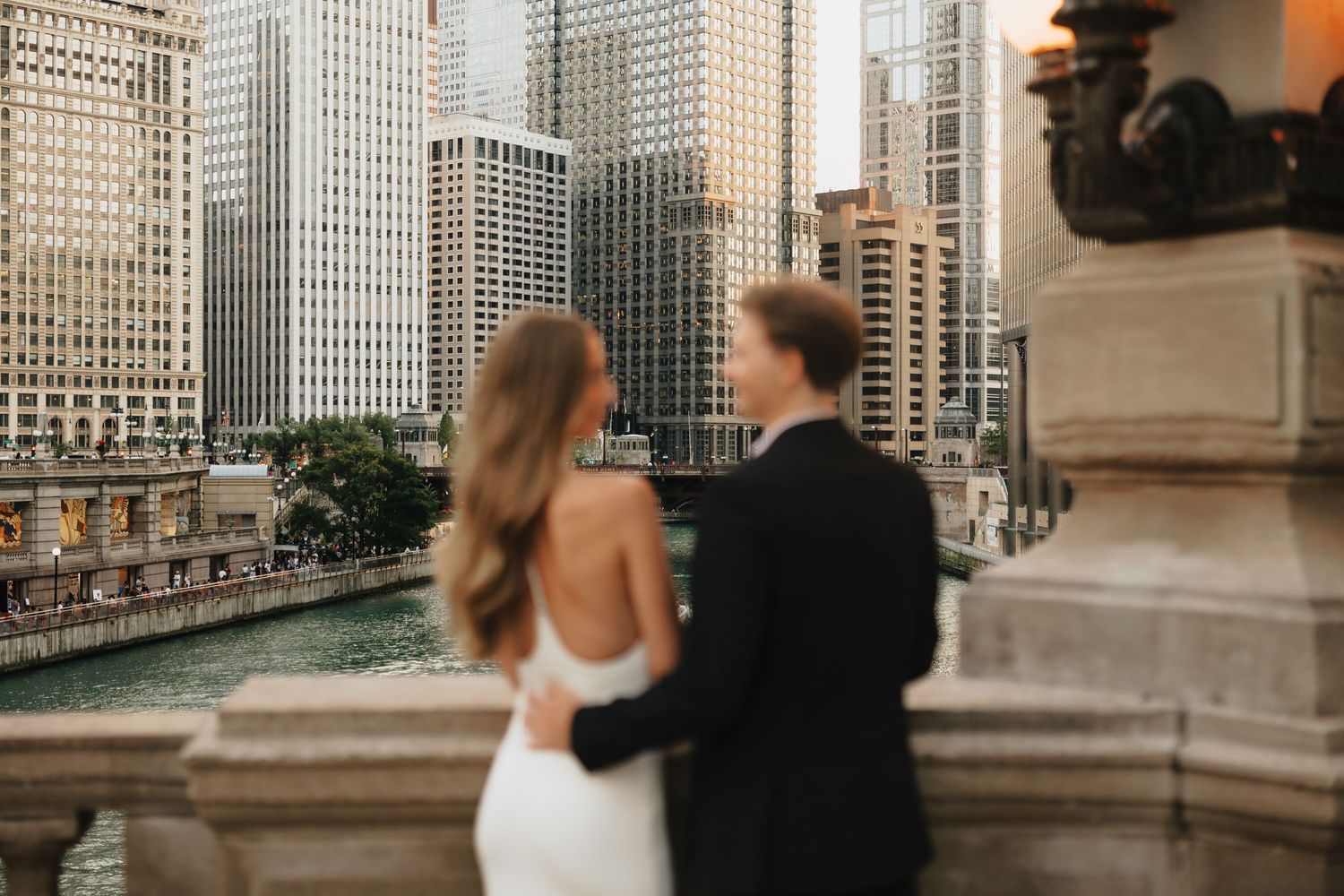 Couple in wedding attire embracing on a balcony overlooking the Chicago River and city skyline.
