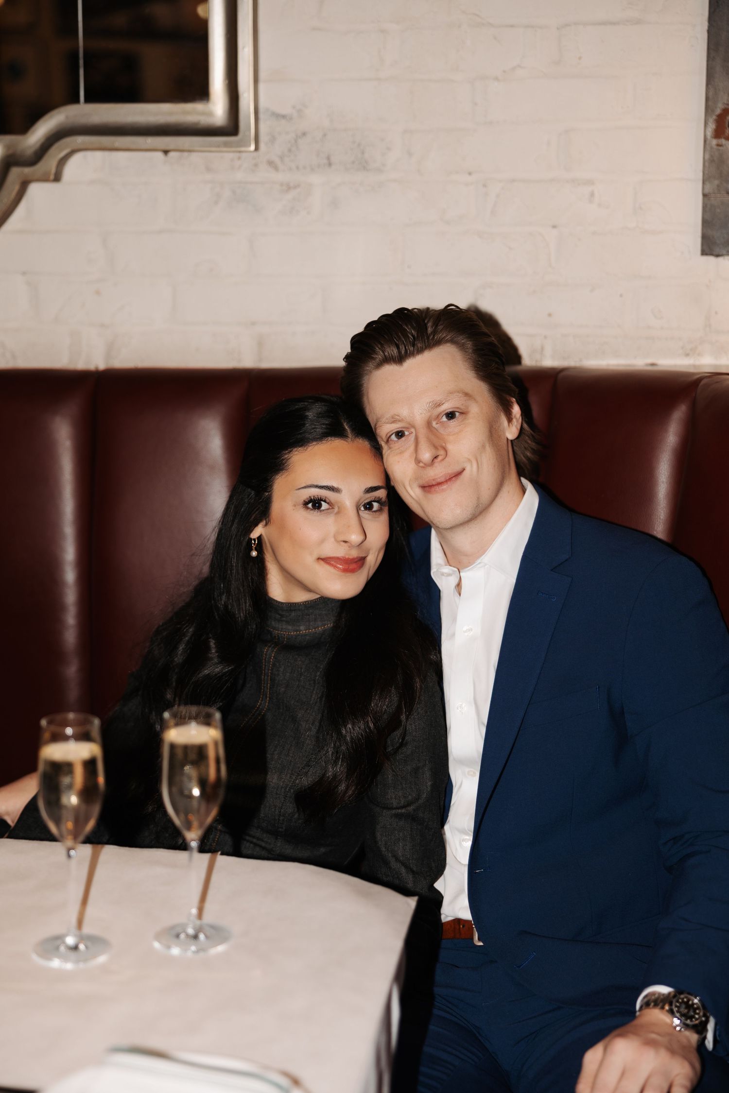 A couple sits together in a cozy restaurant booth with champagne glasses on the table.