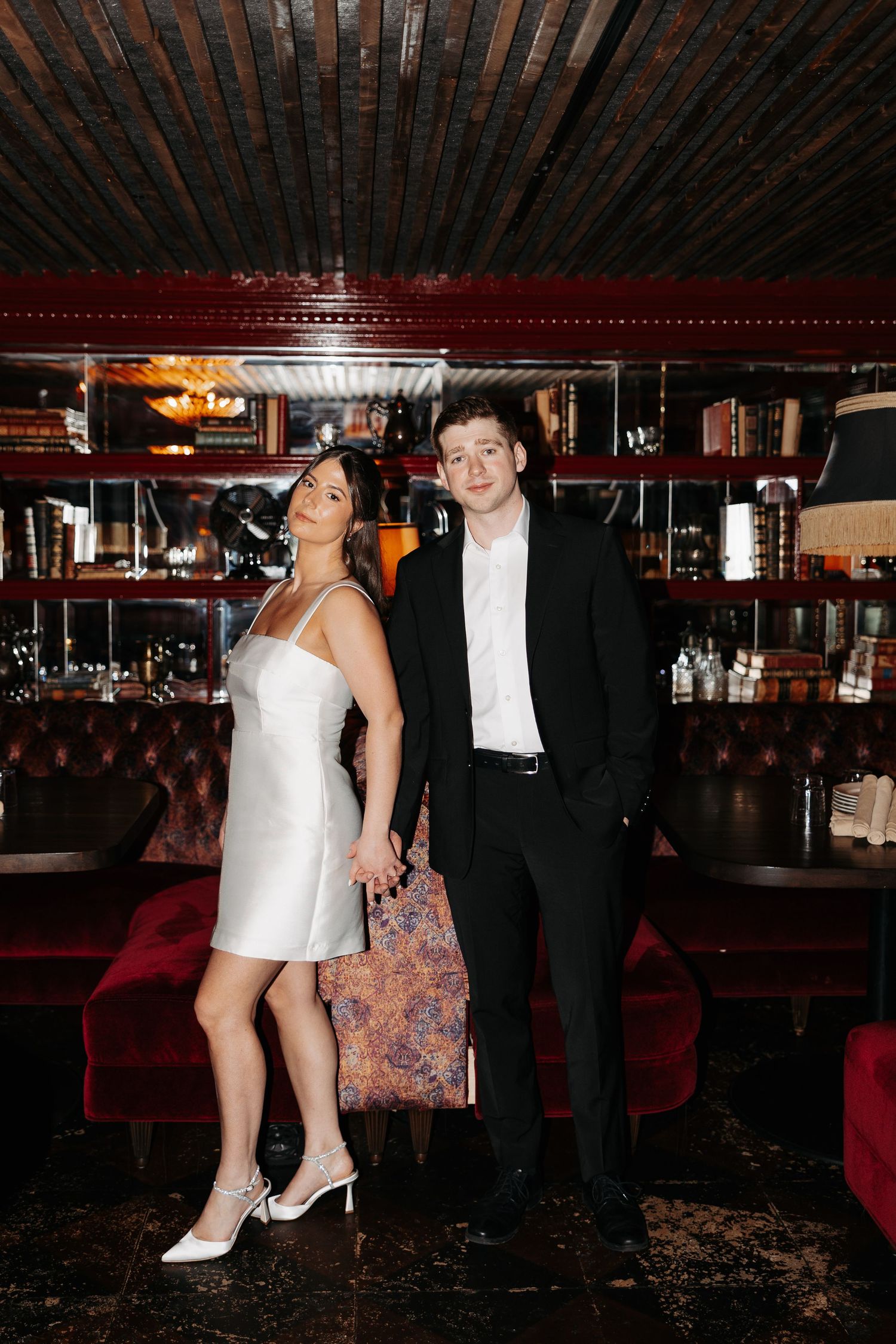 A formal event scene showing people in elegant attire under warm lighting with wood-beamed ceiling.