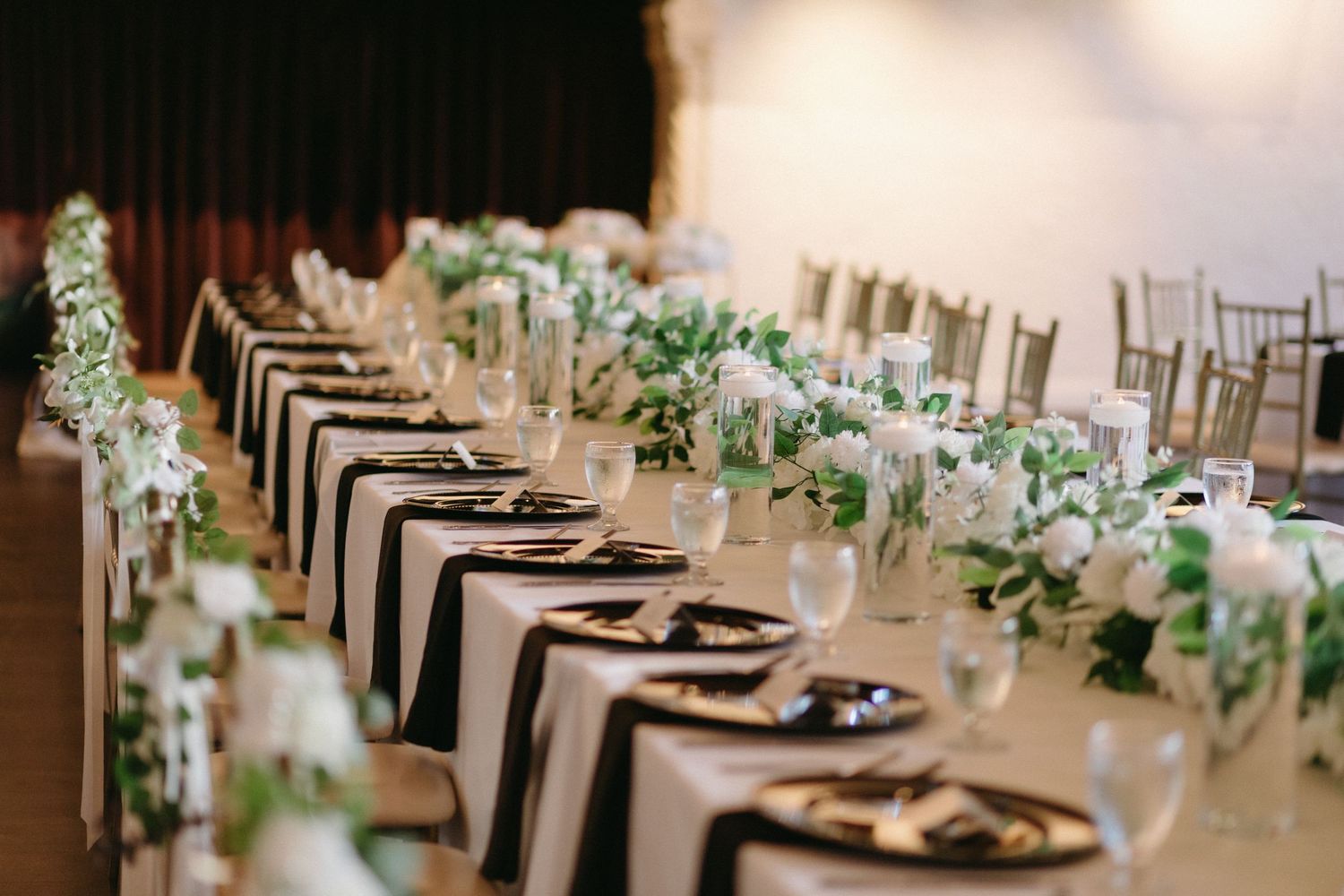 Elegant wedding reception tables set with white linens and greenery centerpieces.