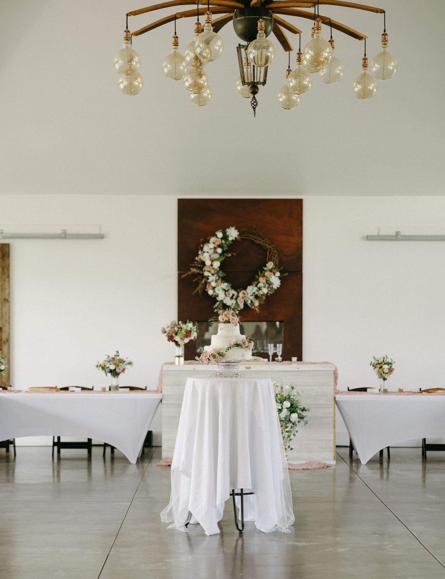 An elegant white wedding reception venue with round tables and chandeliers.