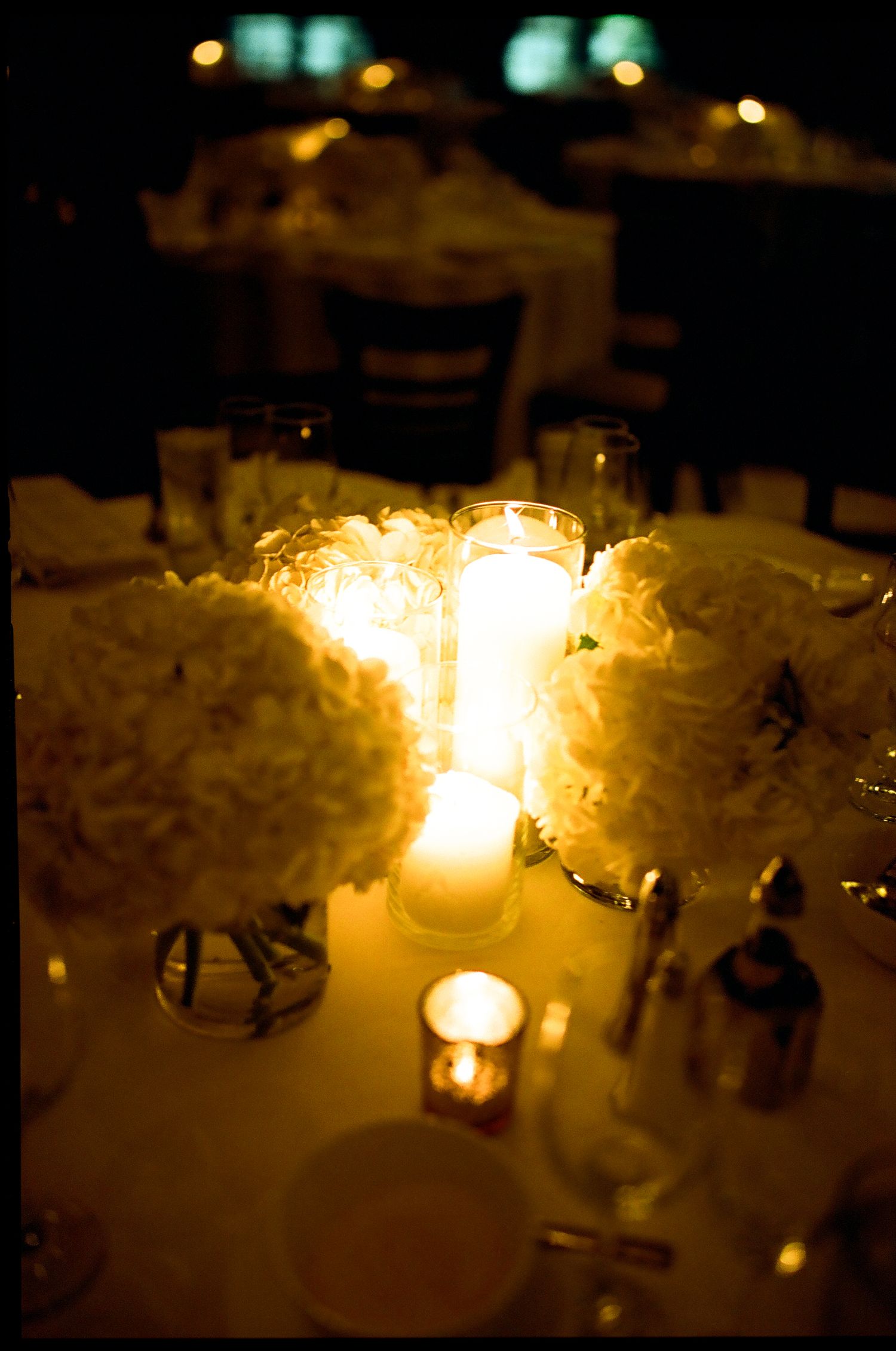 Romantic wedding reception table with glowing pillar candles and white hydrangea floral centerpieces.