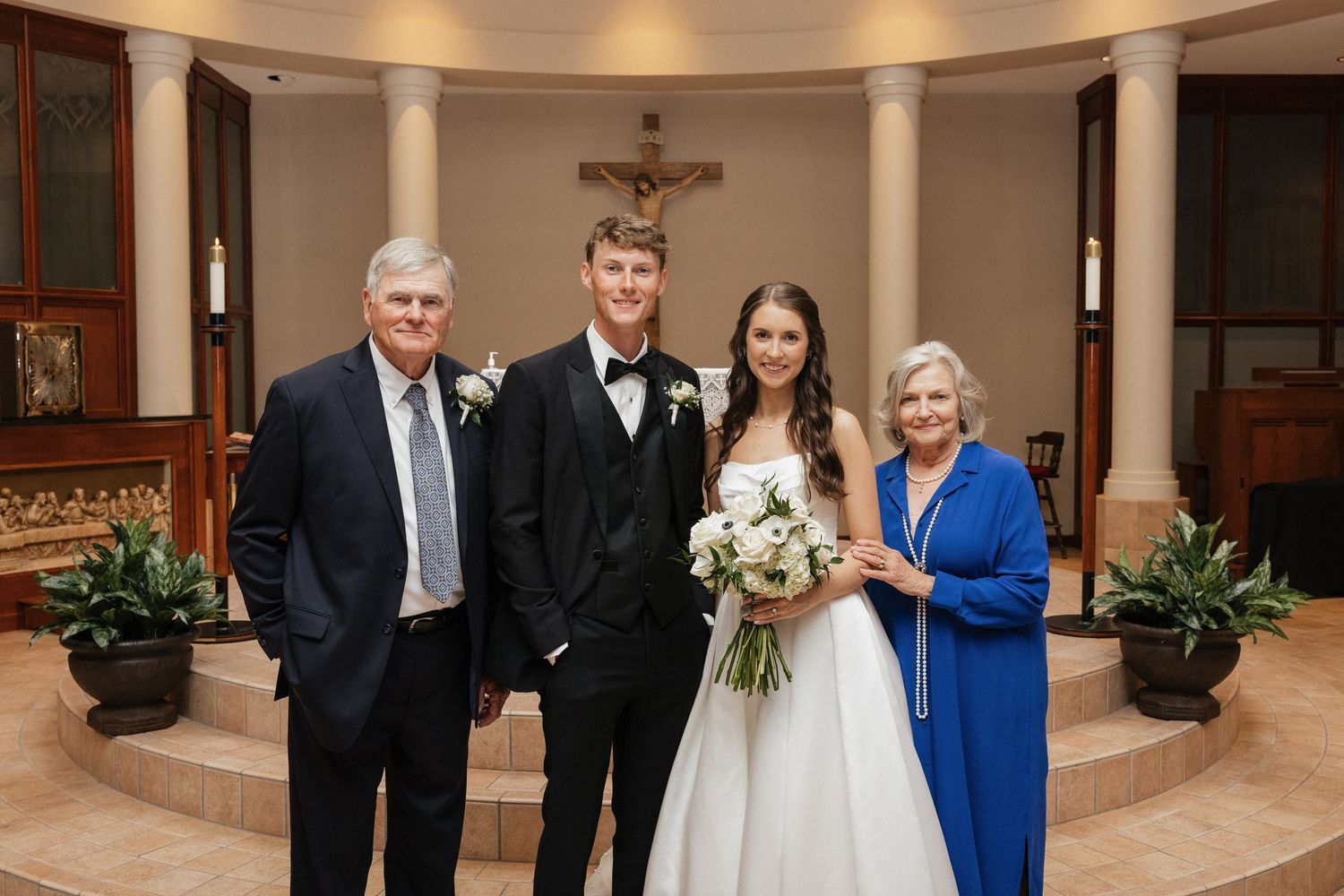 Bride and groom pose with family in a church after their wedding ceremony, bride holding white bouquet.