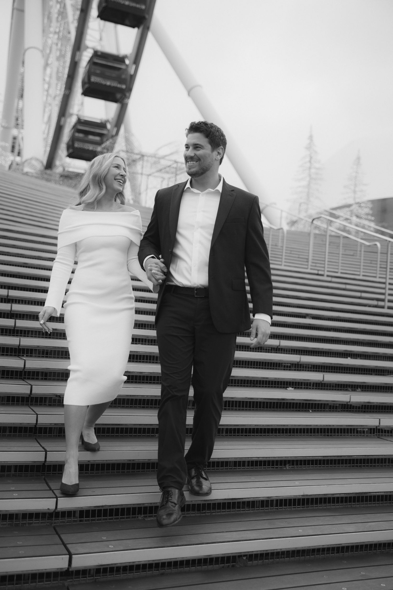 A couple walks down concrete steps in black and white, showing a sequence of playful moments together.