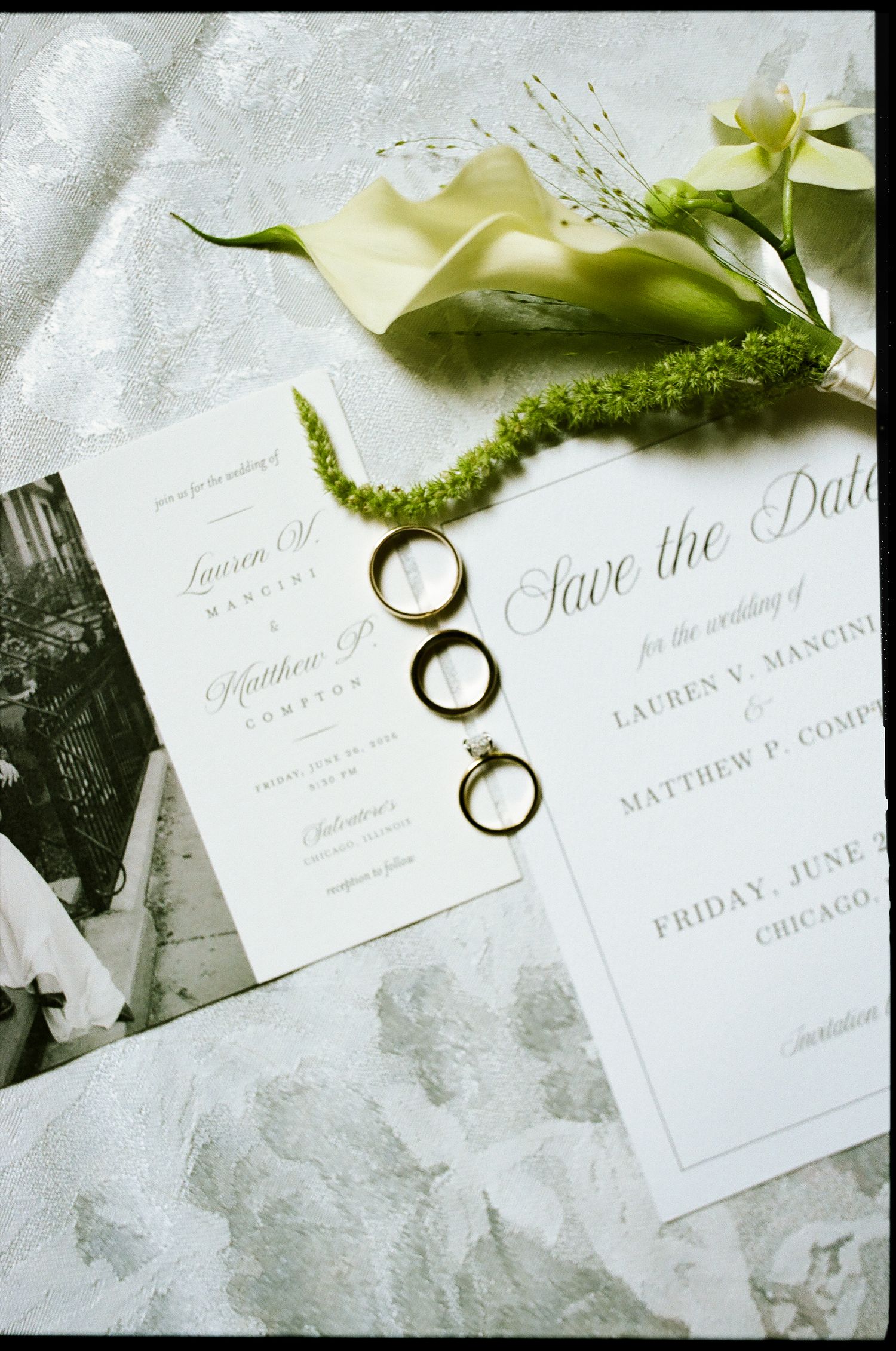Wedding flat lay featuring save the date cards, gold rings, and white calla lily on silver fabric in Chicago.