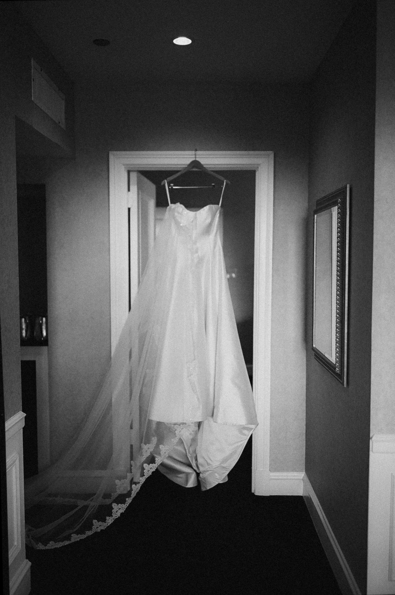 White wedding gown with veil hanging in hotel hallway, black and white photography.