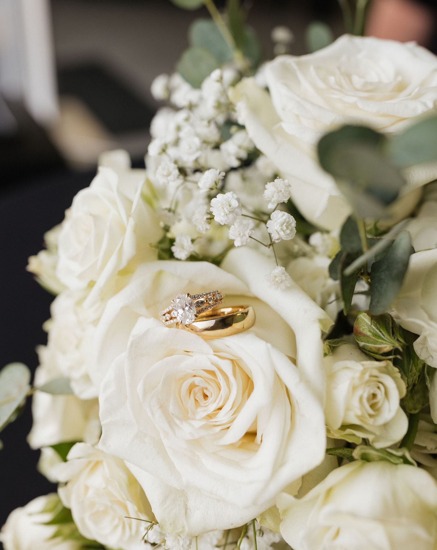 Close up of white roses in a wedding bouquet with engagement and wedding rings.