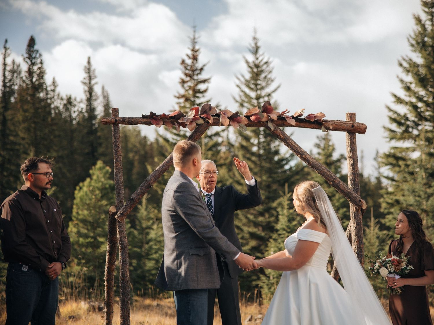 Rustic outdoor wedding ceremony under wooden arch with mountain backdrop.