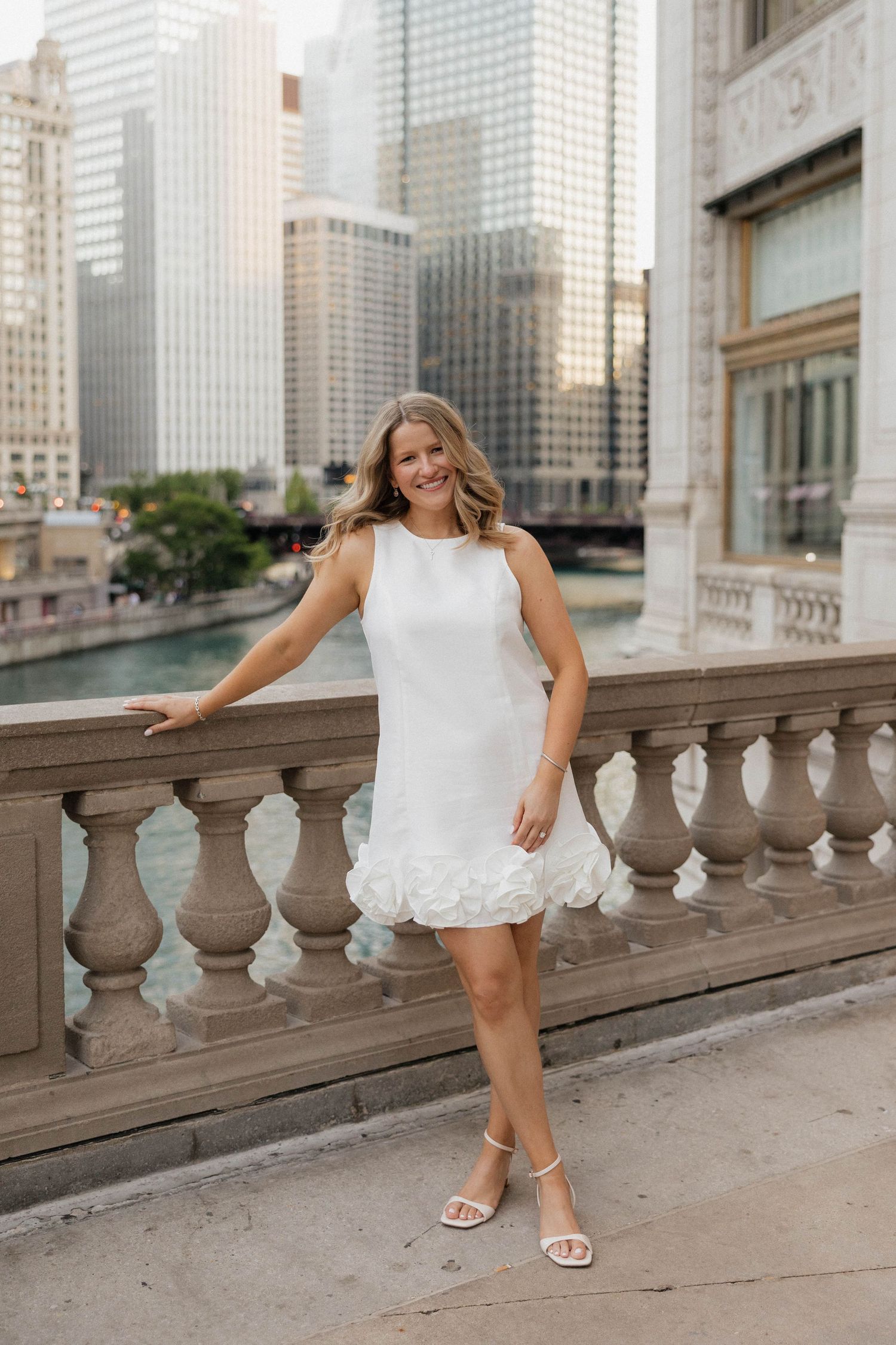 Woman in white ruffled mini dress posing on a balcony overlooking the Chicago River.