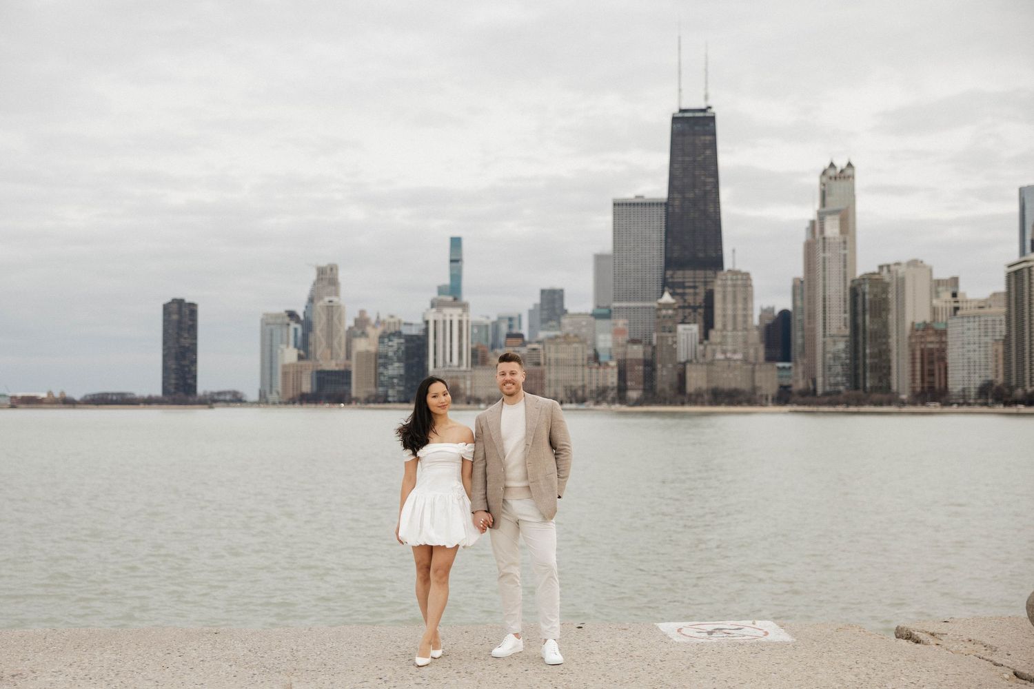 Engaged couple posing on lakefront pier with iconic Chicago city skyline behind them.