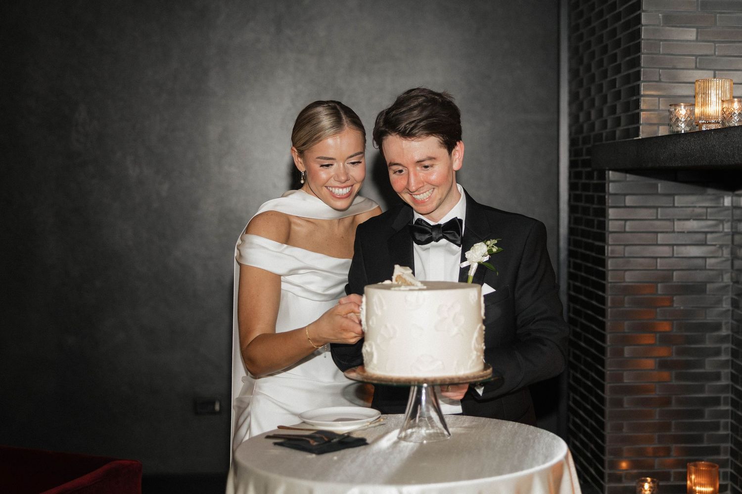 Bride and groom smiling while cutting their elegant white wedding cake at their reception.