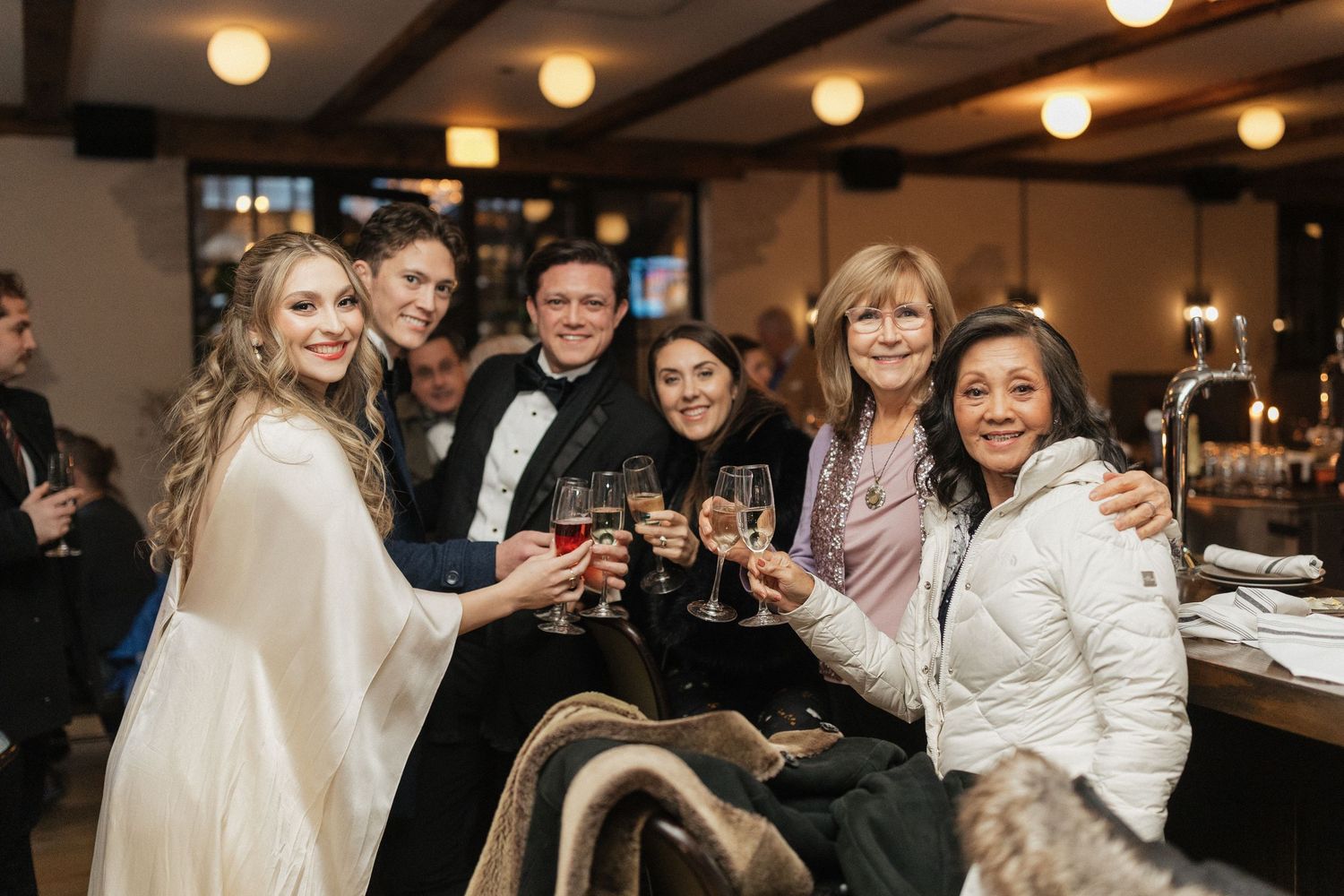 Wedding celebration with guests toasting at a cozy reception venue with warm lighting.