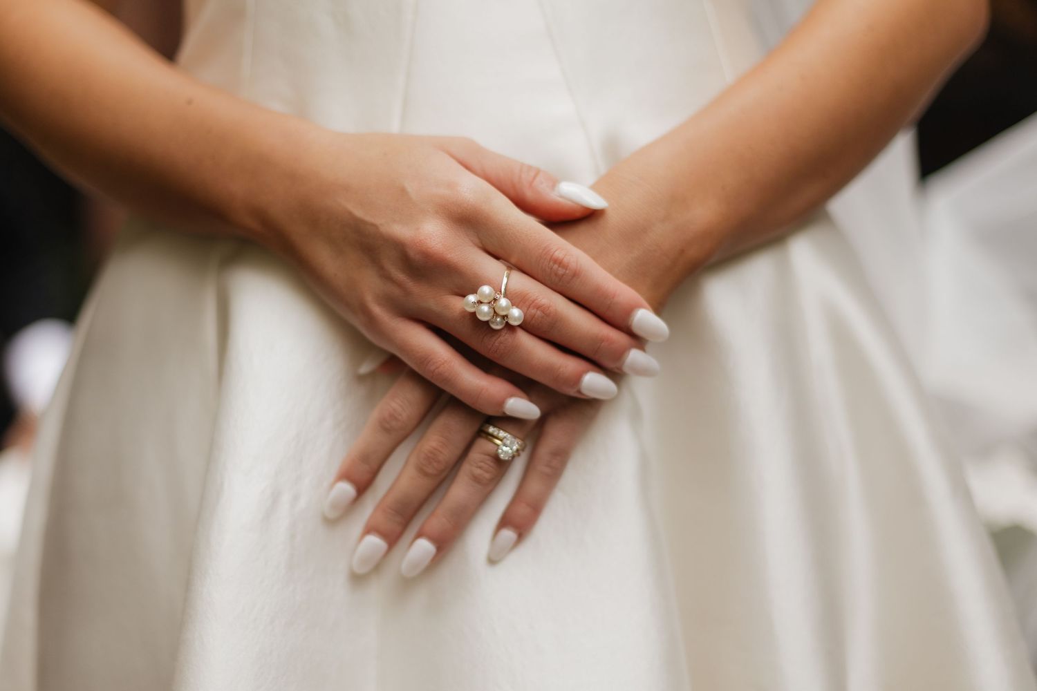 Bride in a white wedding dress with hands gently clasped at her waist, showing an elegant ring and a manicure with soft neutral nails.