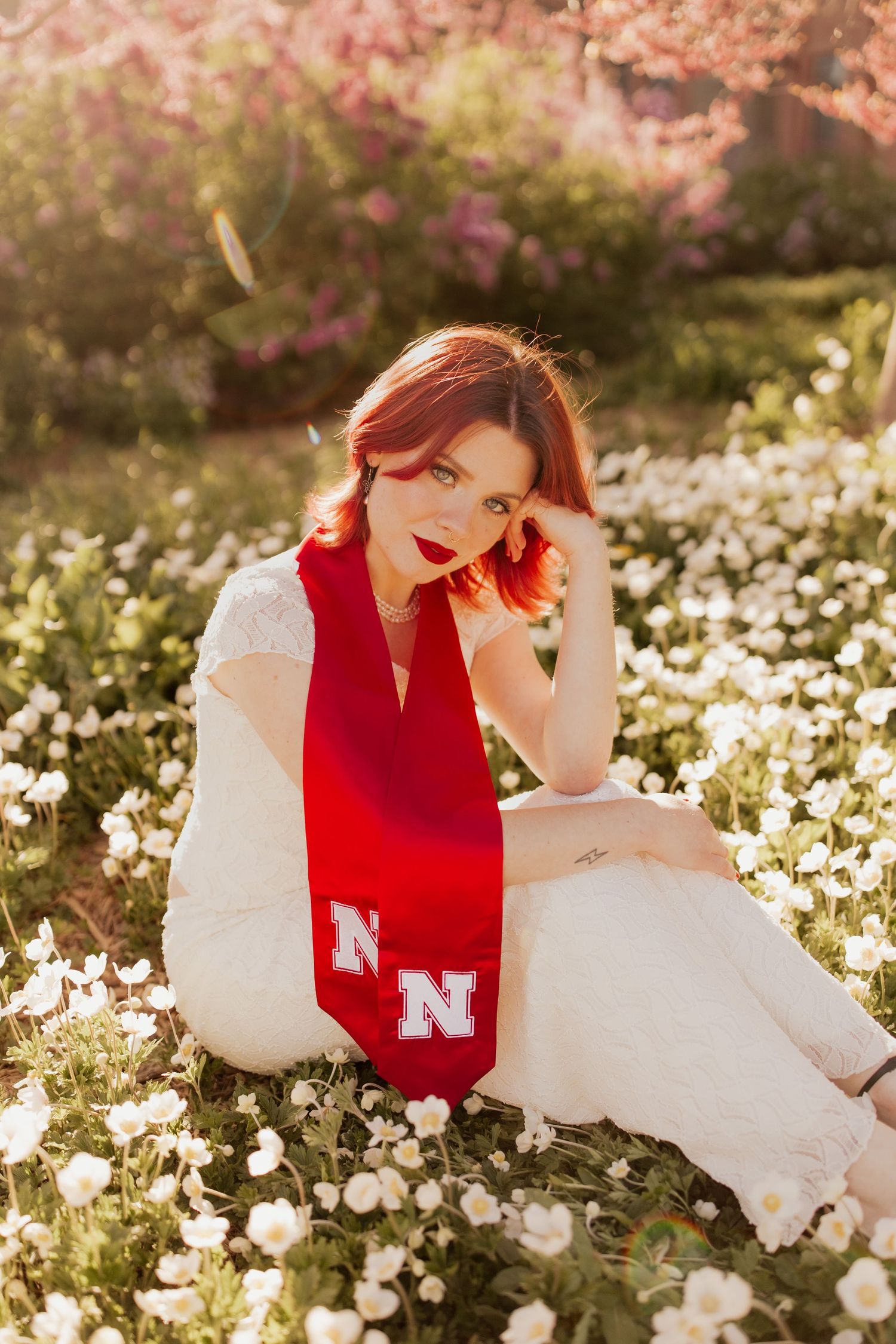 A person in a red varsity letter sweater reclines in a field of white wildflowers during golden hour.