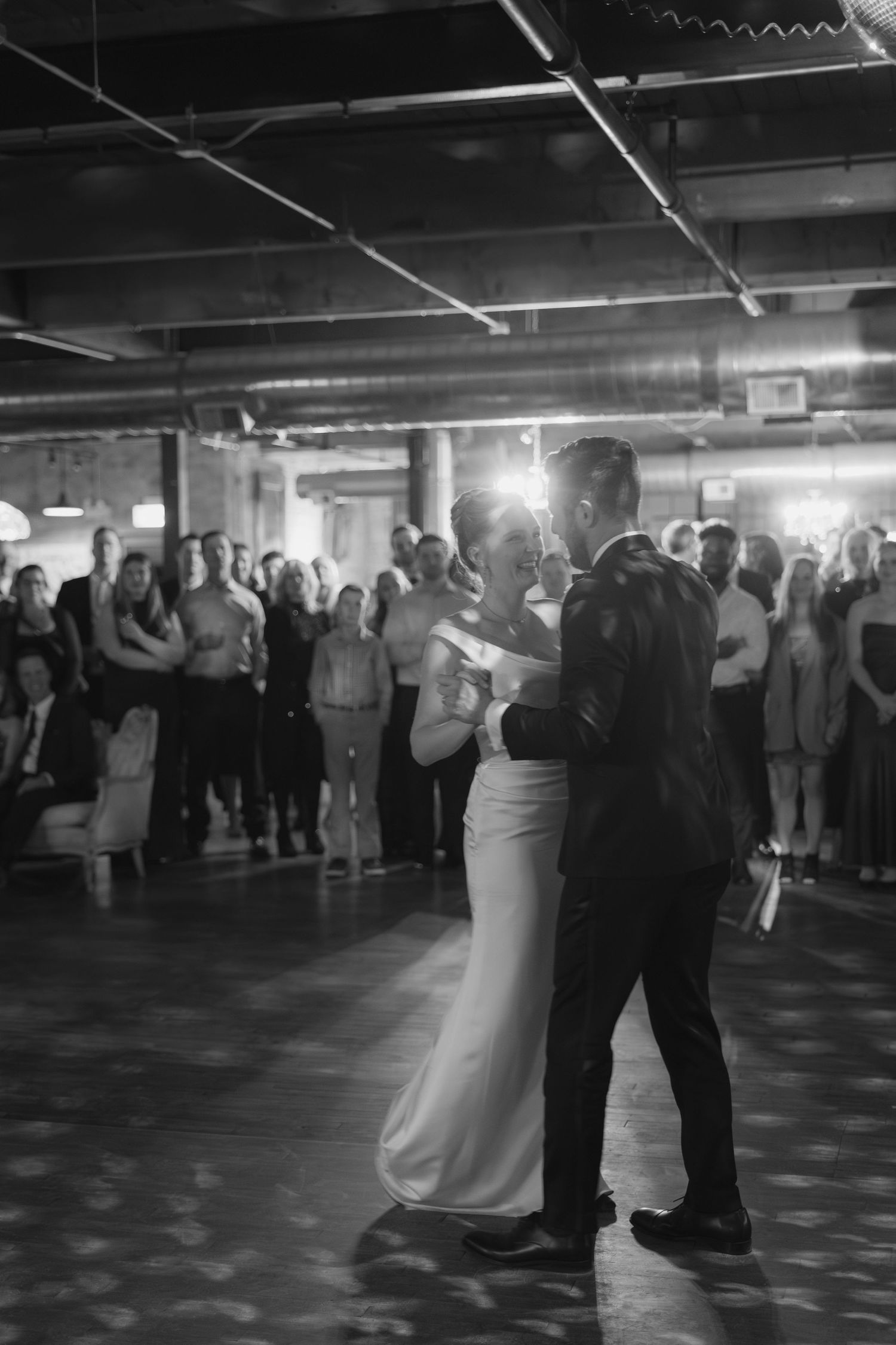 Wedding reception dance floor with couples slow dancing in a dimly lit venue.